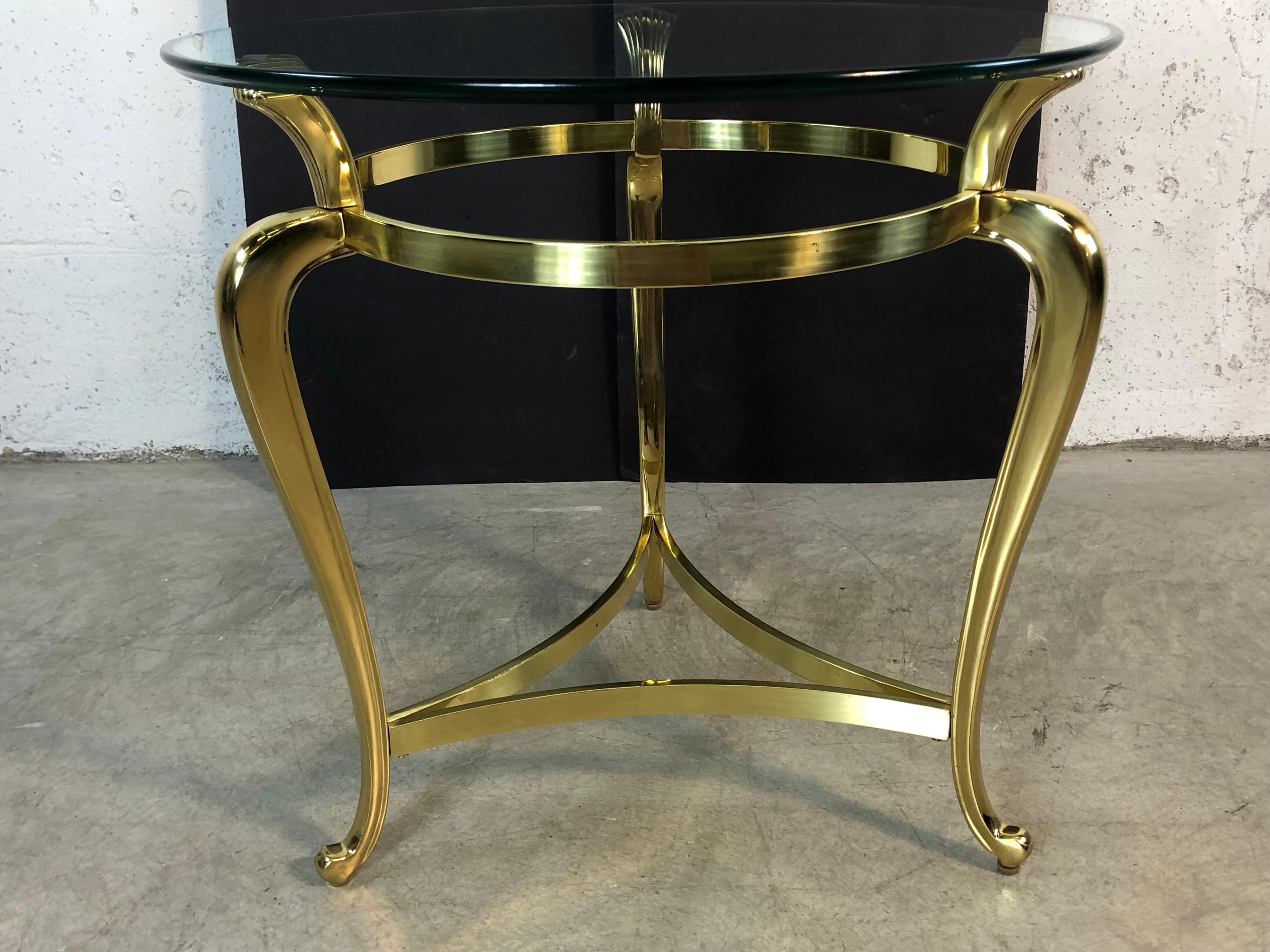 Hollywood Regency round brass base table with a glass top. Table can be used for either a coffee table or an end table. Table has a shell design that holds the glass. Minimal wear to the glass and a couple of spots of tarnish.