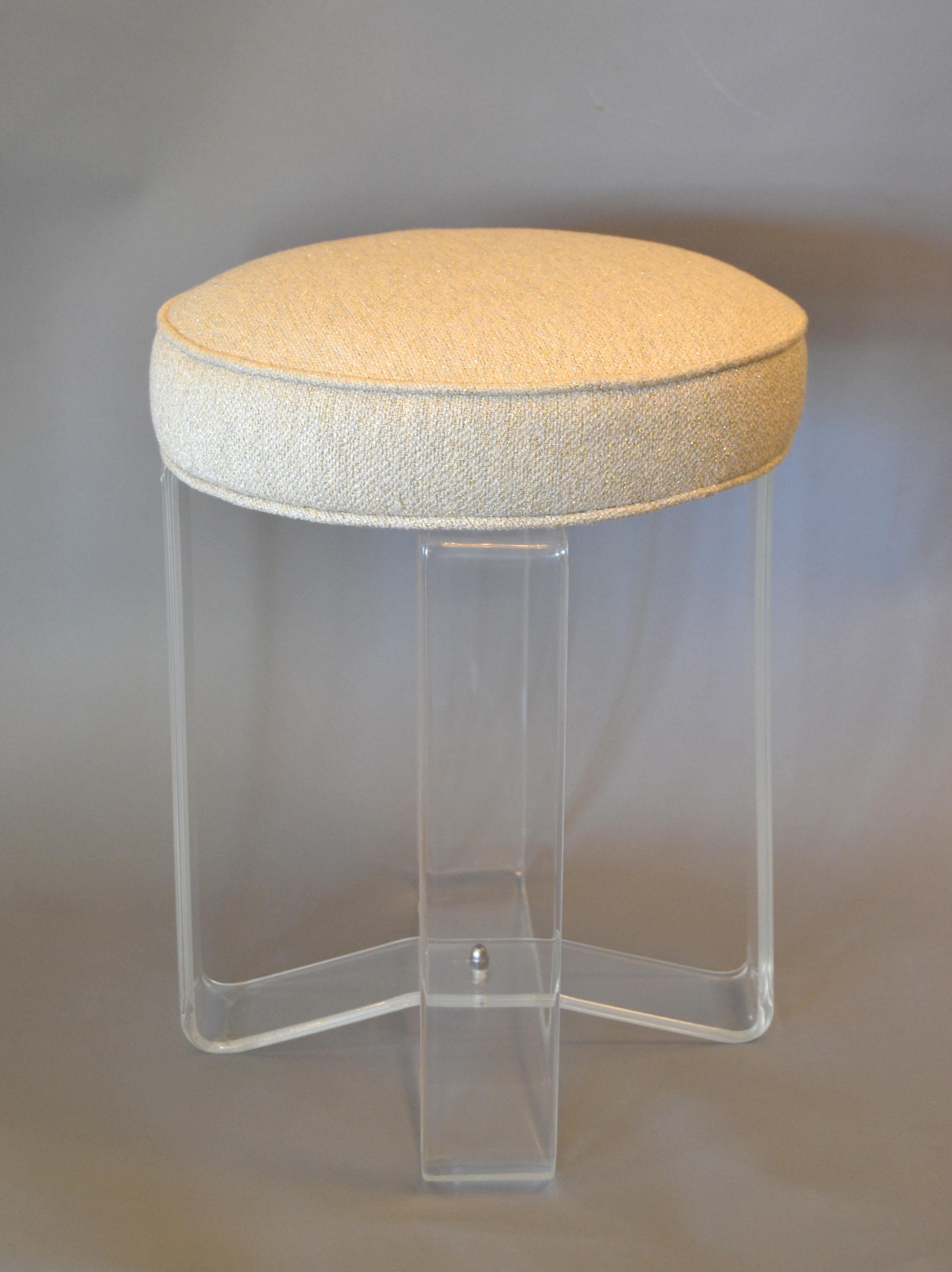 Hollywood Regency round Lucite stool features a transparent base with crissed-cross legs and a cream and gold sparkle boucle fabric upholstered soft seat.
Can be used as an extra seat, vanity stool or footstool.
It is a perfect combination of