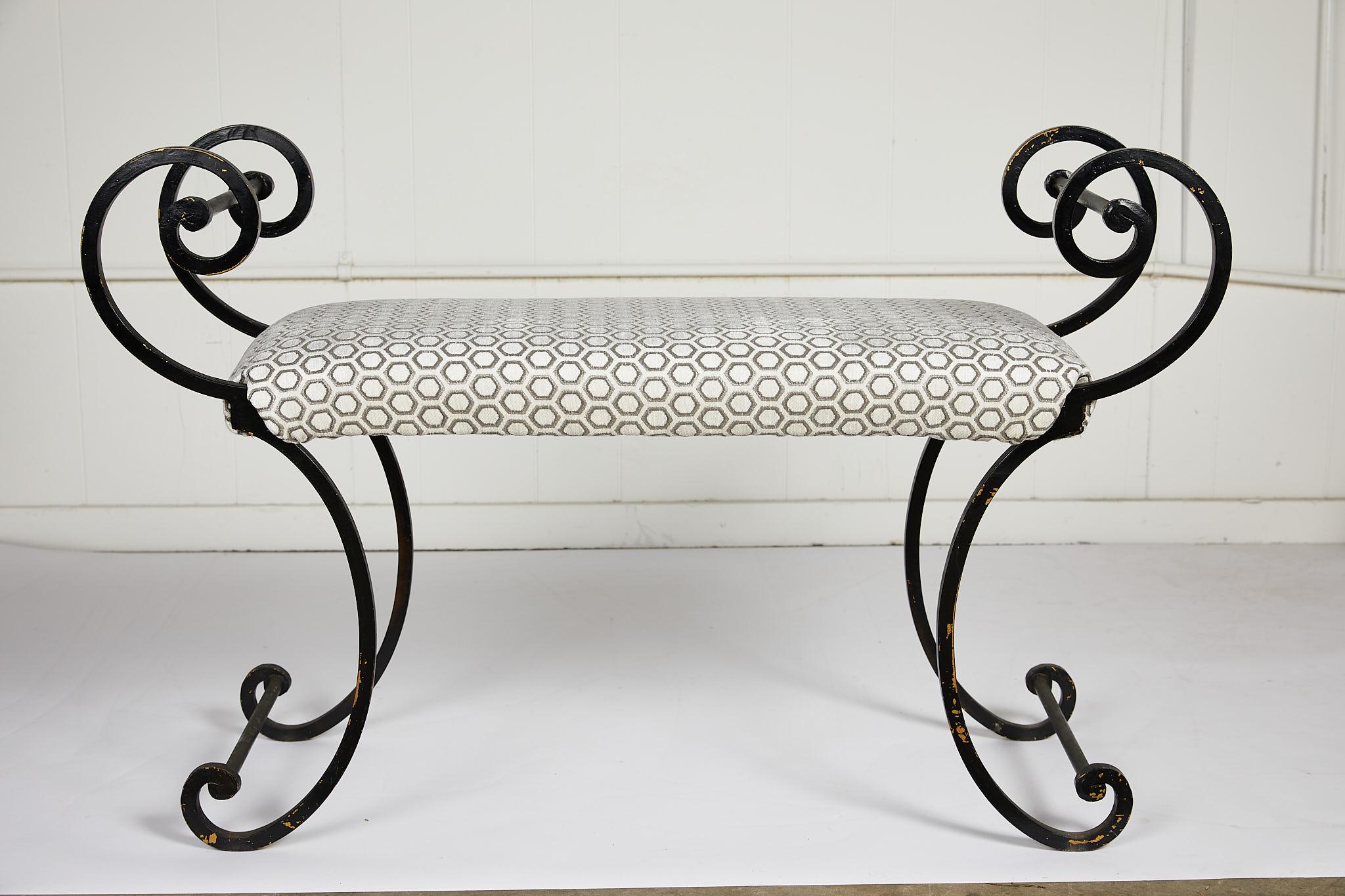 Late 20th century Hollywood Regency style iron bench with elegant scrolling arms and legs supporting an upholstered seat covered in intara ivory by Jim Thompson Fabrics.