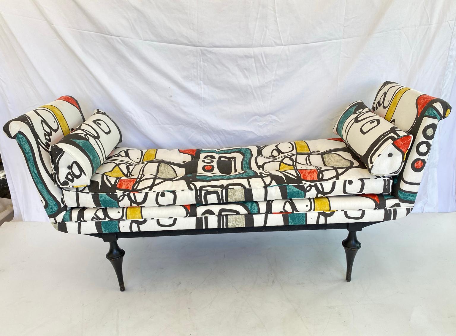 Daybed style settee, upholstered in Joan Miró inspired fabric, having a long, button-tufted, drop-in center cushion, flanked by padded, outscrolled arms, and triangular bolster pillows, on a black lacquer frame, raised on highly stylized, turned