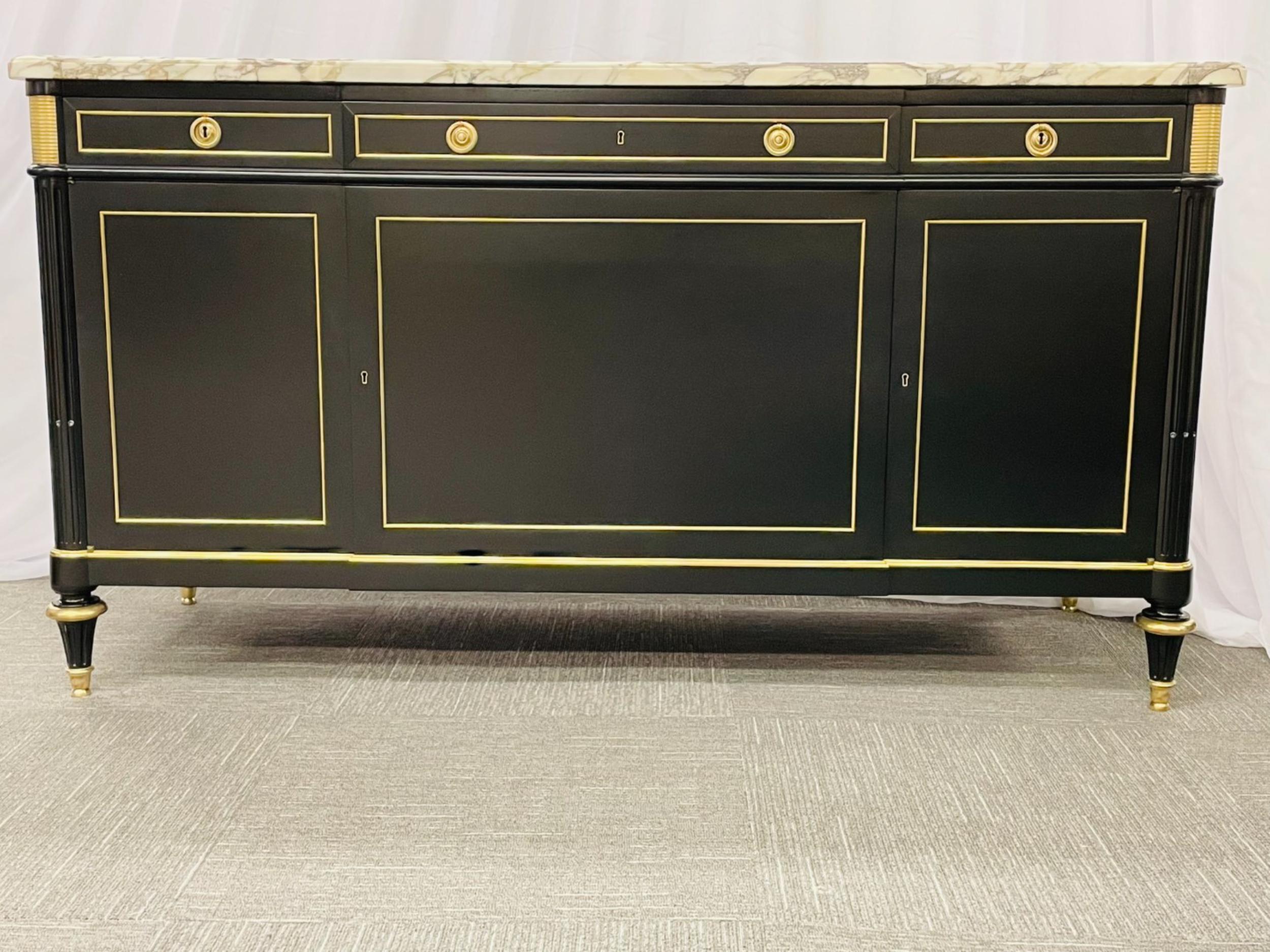 A Louis XVI Maison Jansen Style sideboard or cabinet having an ebony finish with bronze mounts throughout supporting a thick white and gray veined Carrera marble top. This one of a kind wide and fine quality cabinet sports separate key locks for