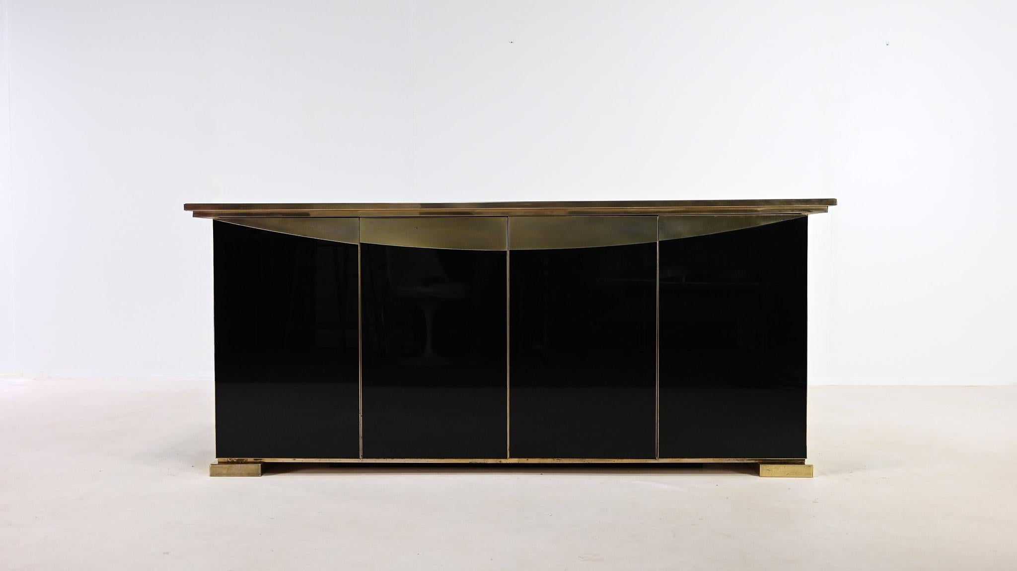 Magnifique buffet de style Hollywood Regency, fabriqué en Belgique dans les années 70. Réalisée en laiton, acier doré et miroir noir, elle s'ouvre par quatre portes dévoilant deux étagères réglables. Petites traces d'usage et patine du temps, très