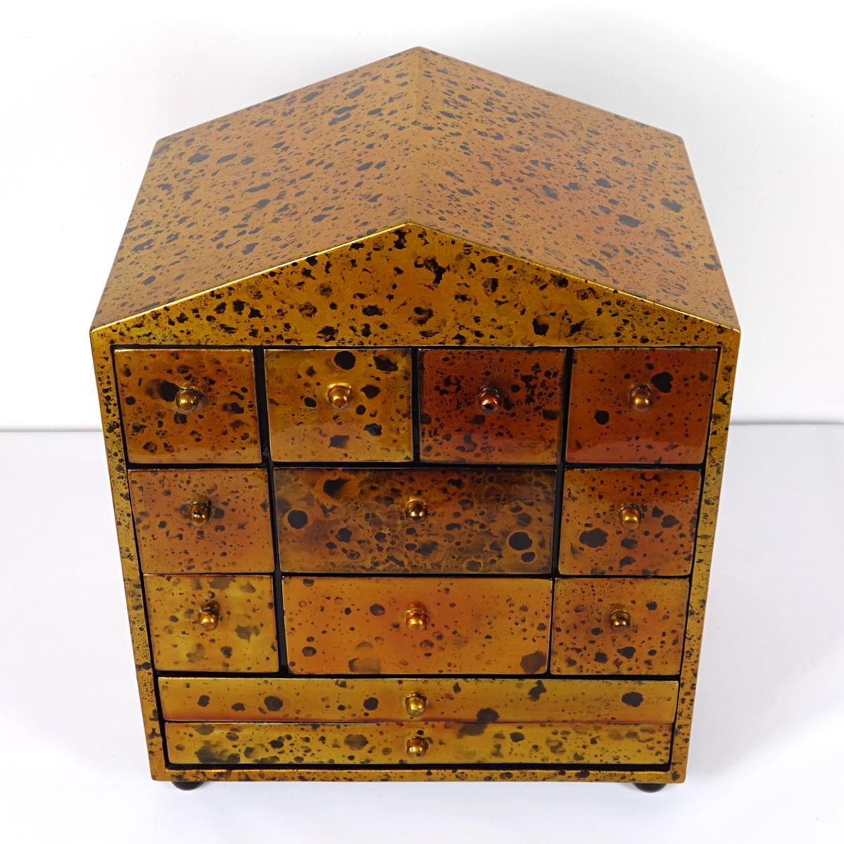 The little golden house of the Waltons... It's as if John-Boy personally left prints of his characteristic mole on the cheek. They are scattered all-over this small chest of drawers in the shape of a house that has been gold lacquered.
This desk or
