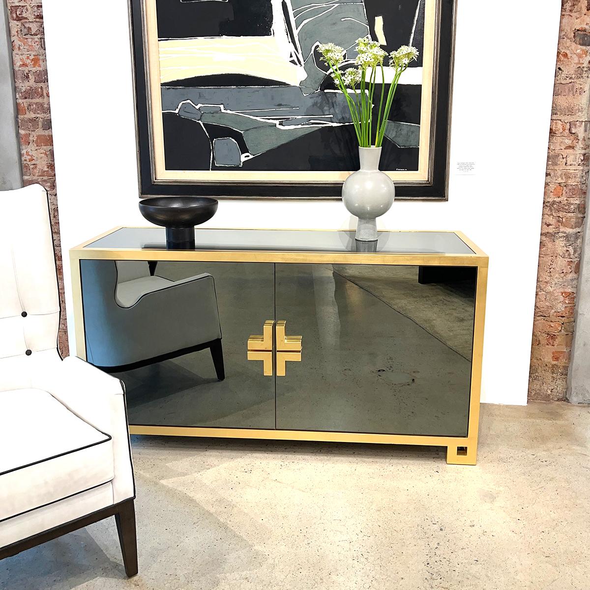 Modern Smoked Mirror Credenza with a gilded frame, two wide doors open to a finished interior with an adjustable shelf. Solid brass accents and handles. The top, sides, and front doors are all smoked mirror glass. 

Dimensions: 67
