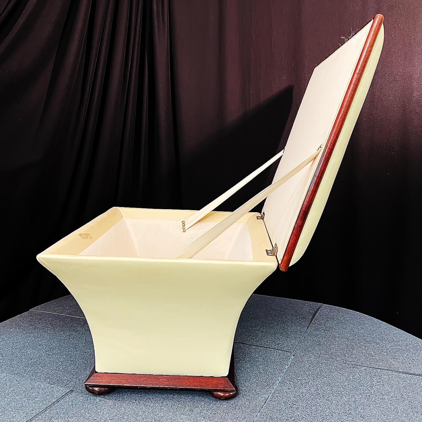 A Hollywood Regency style cream leather upholstered sarcophagus form bench with a lift top and interior storage compartment, with wood trim and base and raised on flattened bun feet. circa 1950

Dimensions: 31