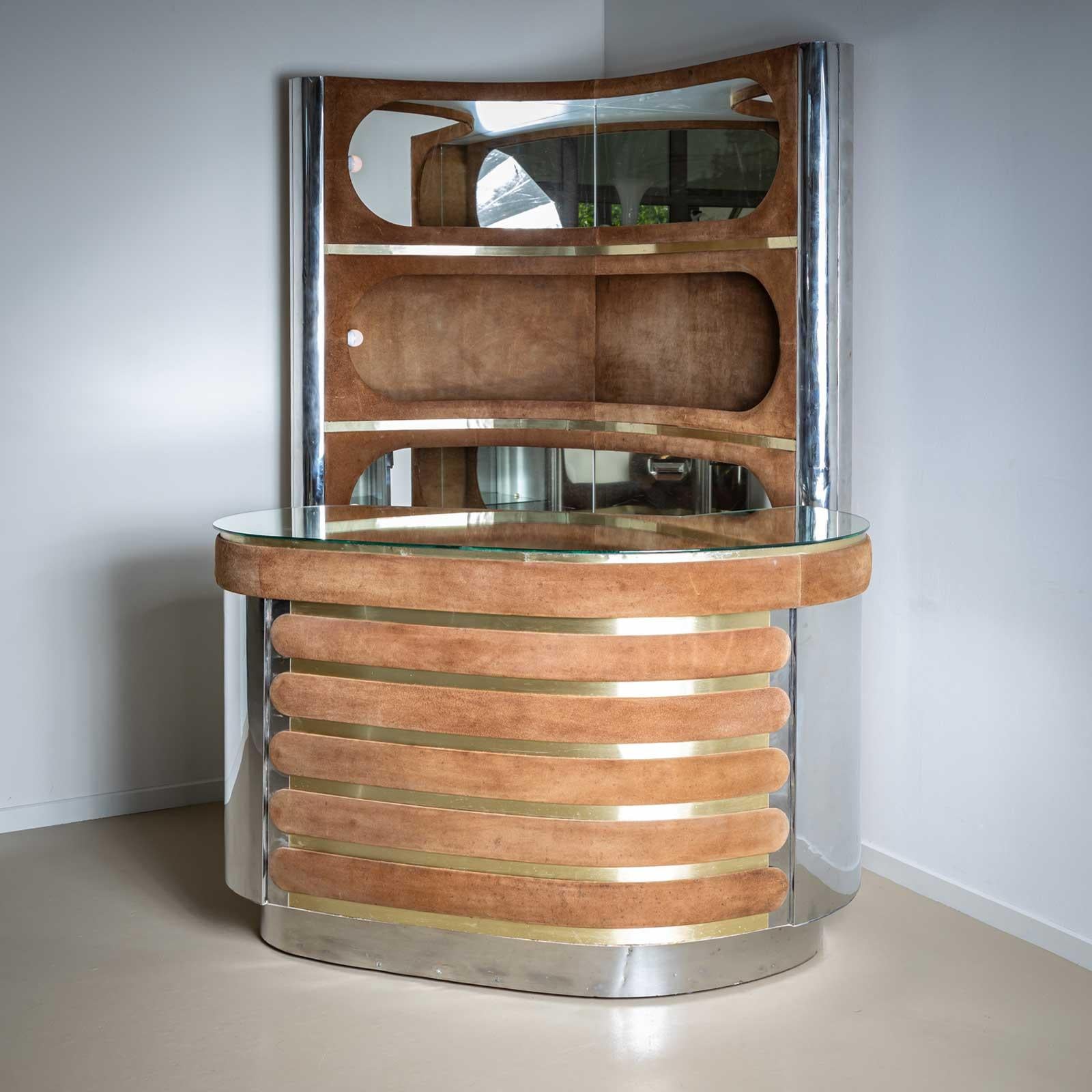 Hollywood Regency style bar with large kidney-shaped counter and L-shaped shelf with integrated lighting and mirrors. The bar is made of polished stainless steel and brass and covered with cognac-coloured suede. The bar is in a restored condition.