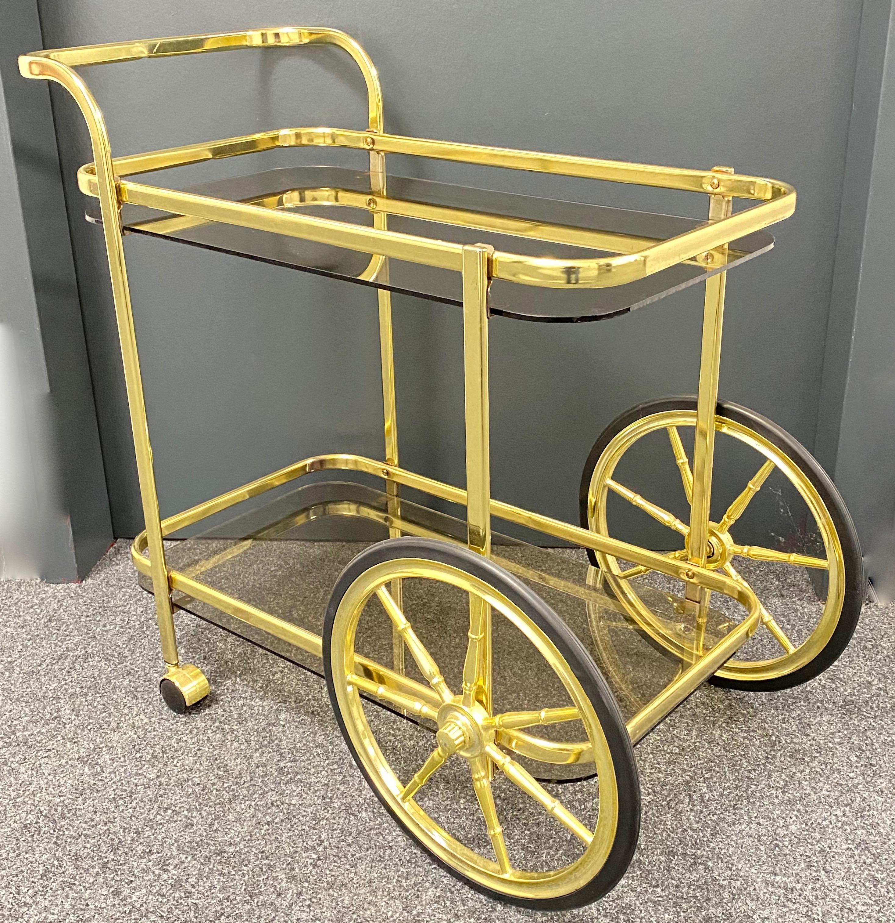Offered is an absolutely beautiful, 1970s bar cart, tea trolley or drinks stand. Two amber or smoked colored glass plates on a brass (finish) metal frame gives this piece a classy statement. A nice addition to every room or a patio.