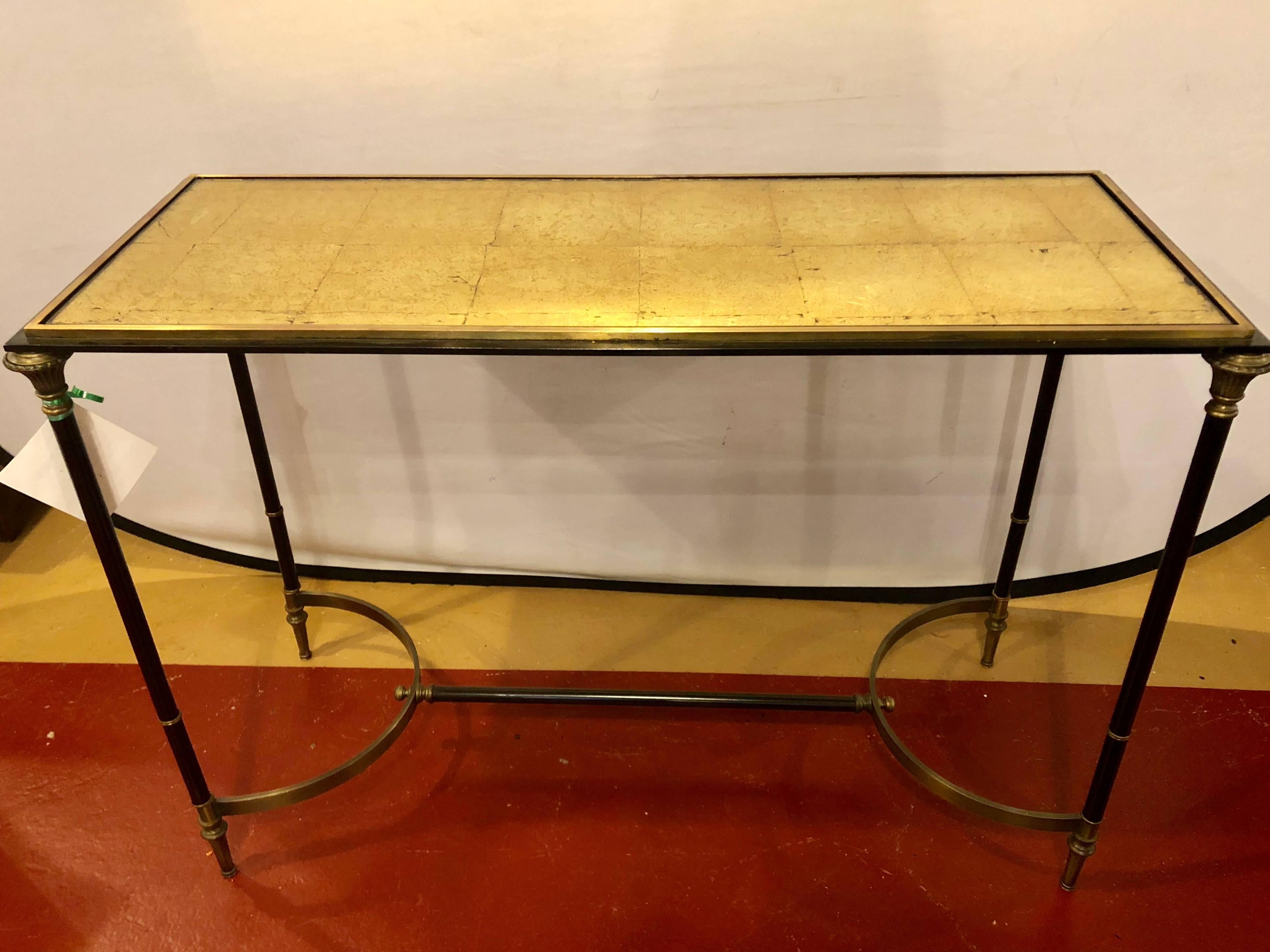 Black and gold console or sofa table in the manner of Maison Jansen. Having a steel ebony and brass base supporting a gilt glass tabletop.