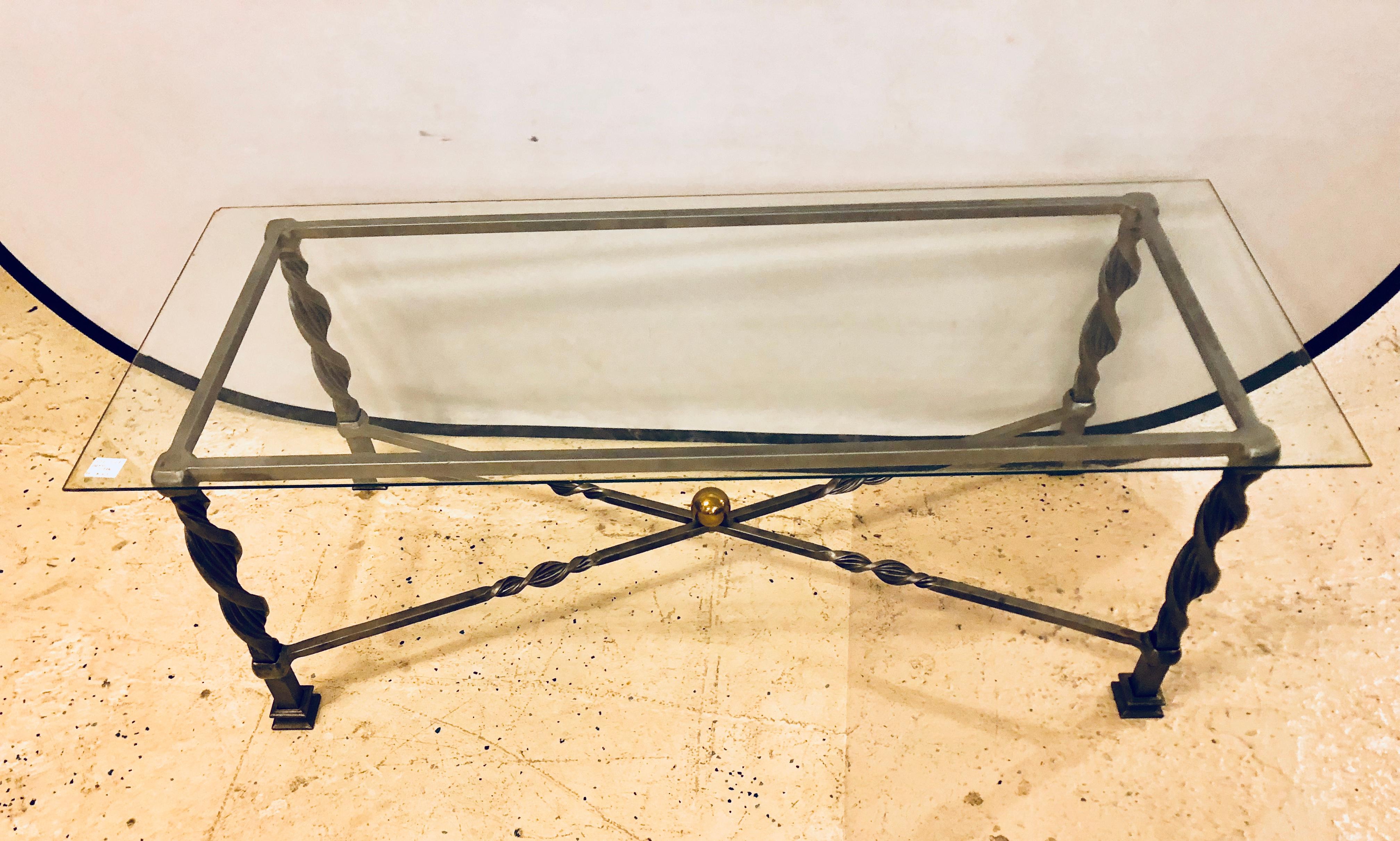 A Hollywood Regency style brass and steel glass top coffee table in the manner of Maison Jansen. This strong and heavy masculine coffee table is twisted steel with brass adornments. 

1XX.