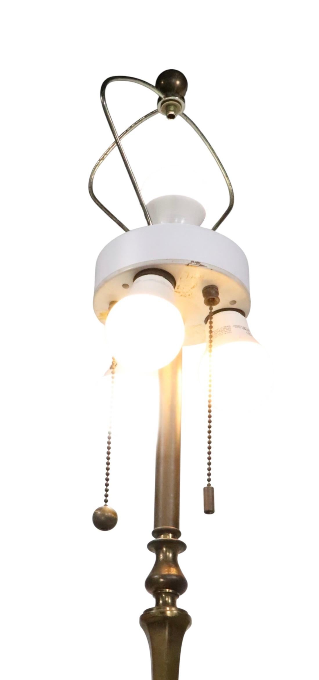 Lampada da terra elegante, sofisticata e di tendenza, caratterizzata da una base con piedi strombati che sostiene lo scultoreo stendardo verticale in ottone. Il piano è configurato con un'insolita sezione inferiore a tre grappoli, con un unico bulbo