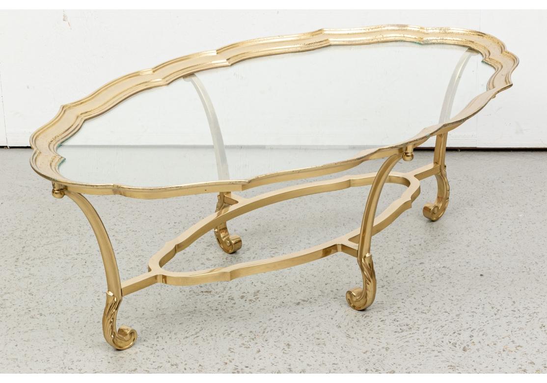 A large oval table with deep serpentine brass frame for the glass top. Mounted on a brass oval serpentine base with stretchers for the incurved scrolled footed legs with leaf details. 
L. 48