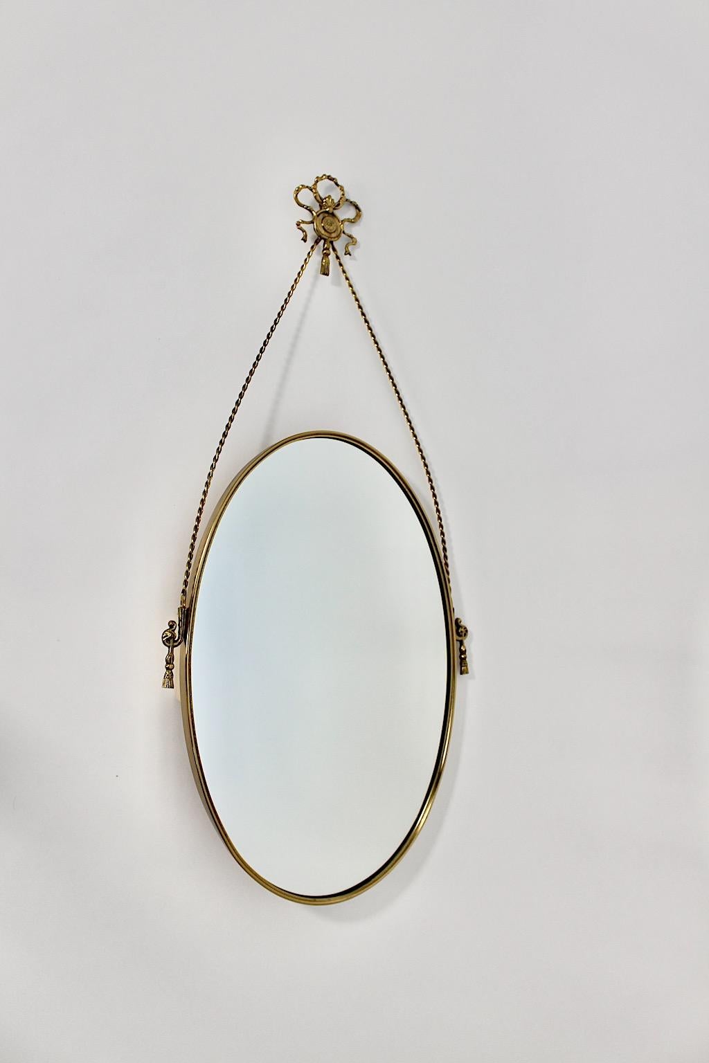 Specchio da parete vintage in stile Hollywood Regency in ottone anni '70.
Un incantevole specchio da parete di forma ovale con bellissimi dettagli in ottone, come le corde e le nappe in ottone, il papillon in ottone e le rosette in ottone su ogni
