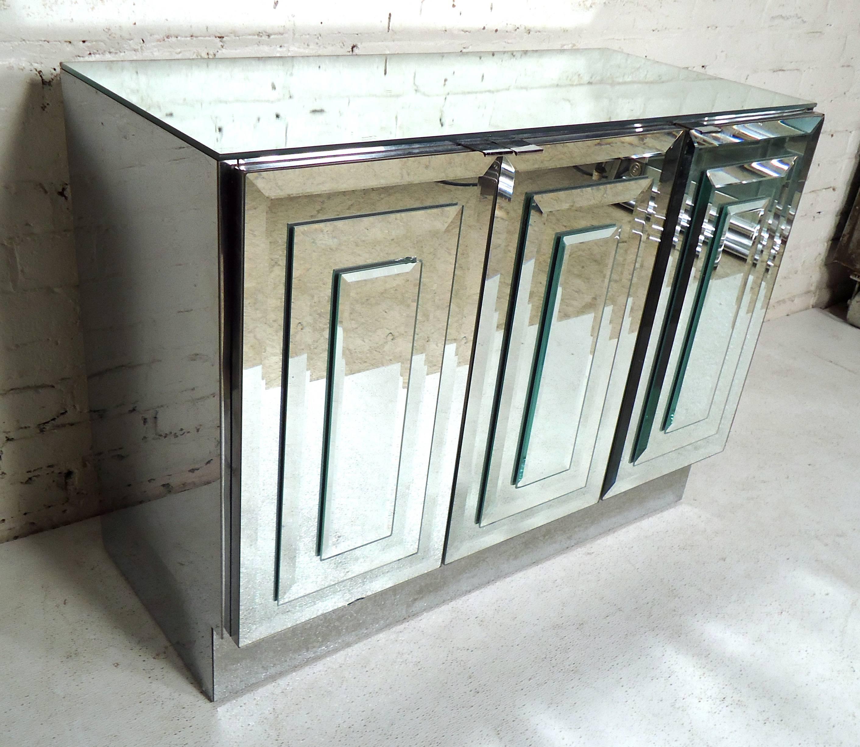 This stylish Mid-Century Modern cabinet features elegant mirrored finish, with sculptural glass fronts and sides. Interior cabinet space offers adjustable shelf storage ideal for bedside or living room use. Please confirm item location (NY or NJ).