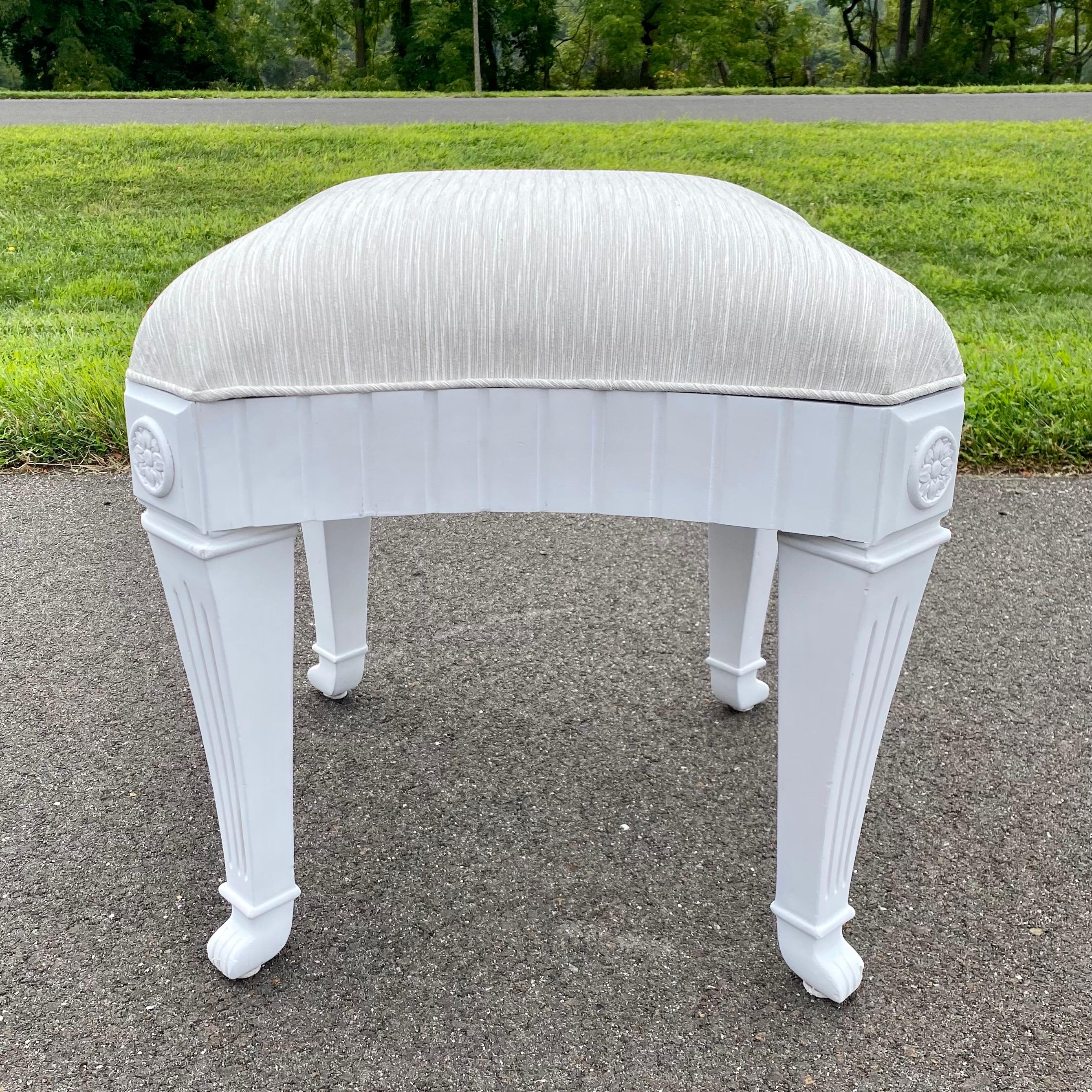 Hollywood Regency style accent stool by Casa Stradivari. This sculptural ottoman or bench features a matte white plaster-like painted wood frame topped with a new upholstered seat in a neutral textured Kravet fabric. Details include Neoclassical