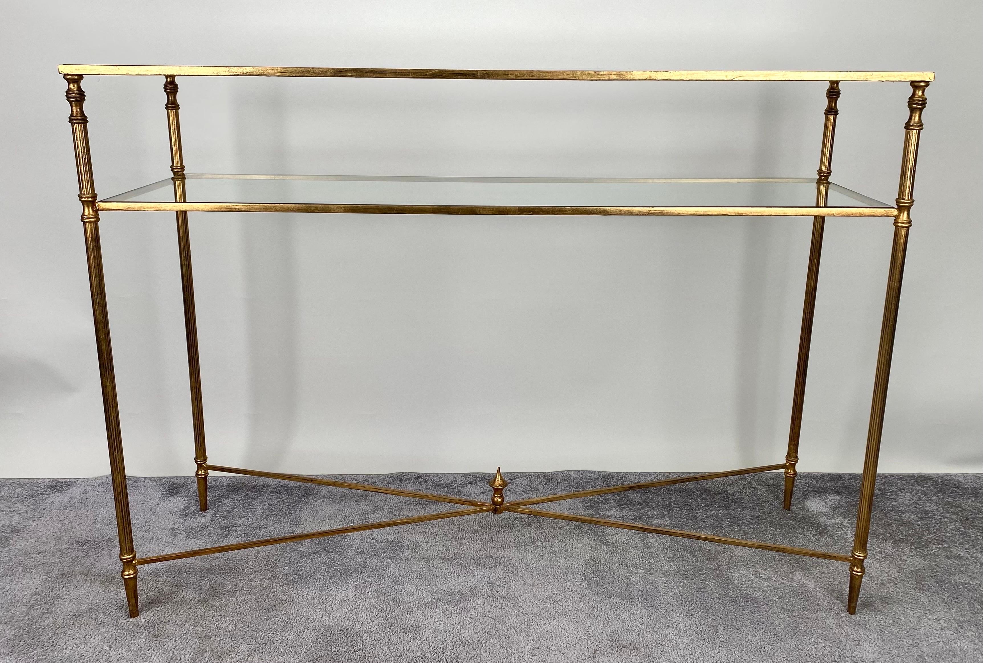 The Hollywood Regency style console features a mirror glass that graces the upper surface, casting a luminous reflection that elevates the ambiance of any space.  This console boasts a singular glass shelf, strategically positioned to harmonize