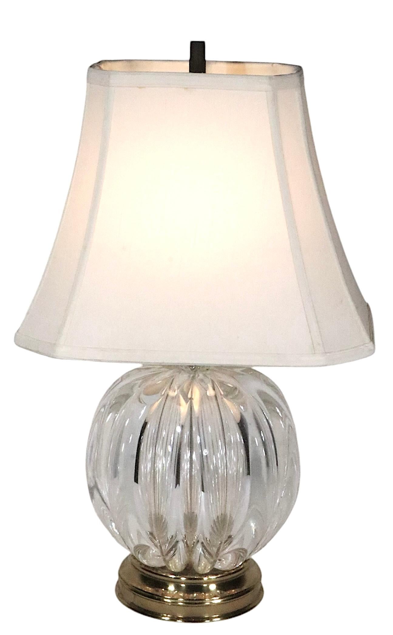Voguish Hollywood Regency style art glass table lamp, consisting of a crystal ribbed ball form body, on a brass plinth base.  This example is in very good, original, clean, and working condition, free of damage or repairs.
Design attributed to