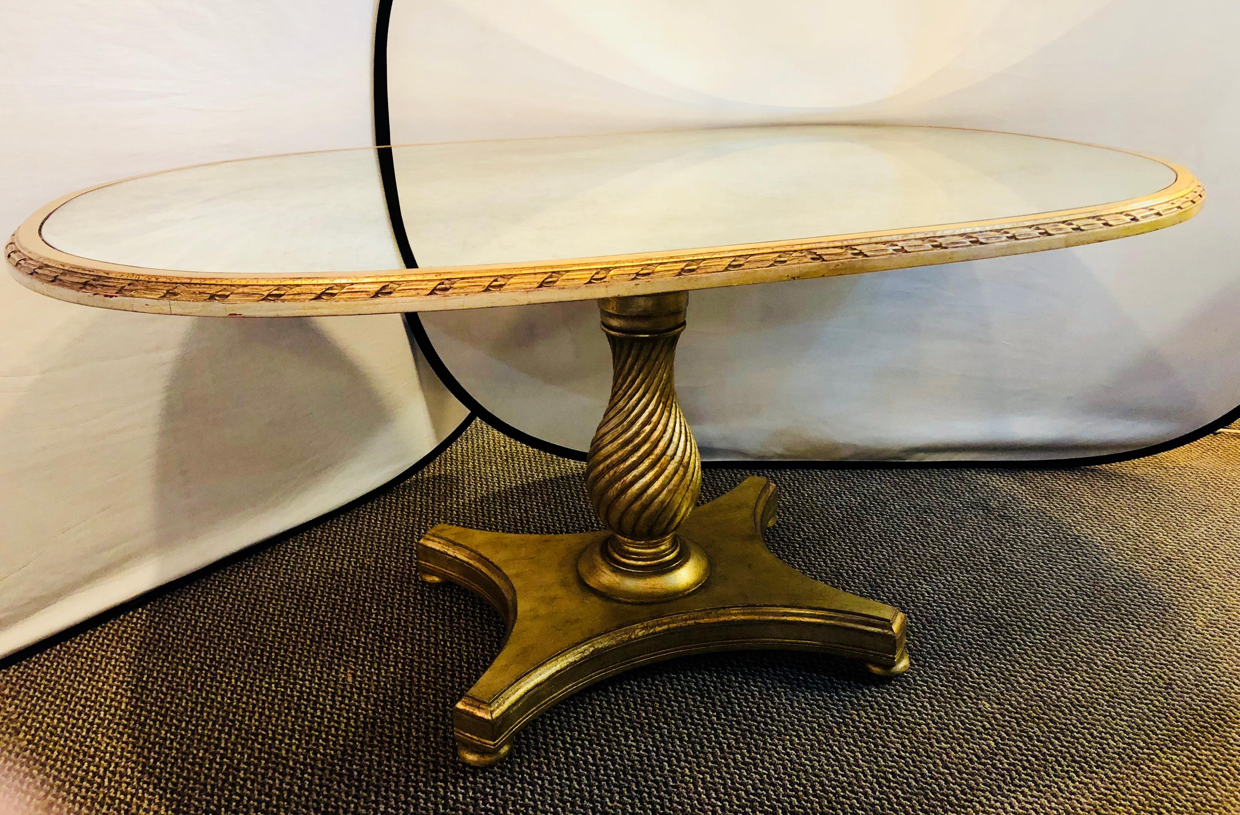 A Hollywood Regency style distressed silver and gold leaf oval pedestal dining table. Having a distressed finish of clay under gilt gold or silver highlights this stunning dining table has a twisted pedestal base and a distressed mirror top. Custom