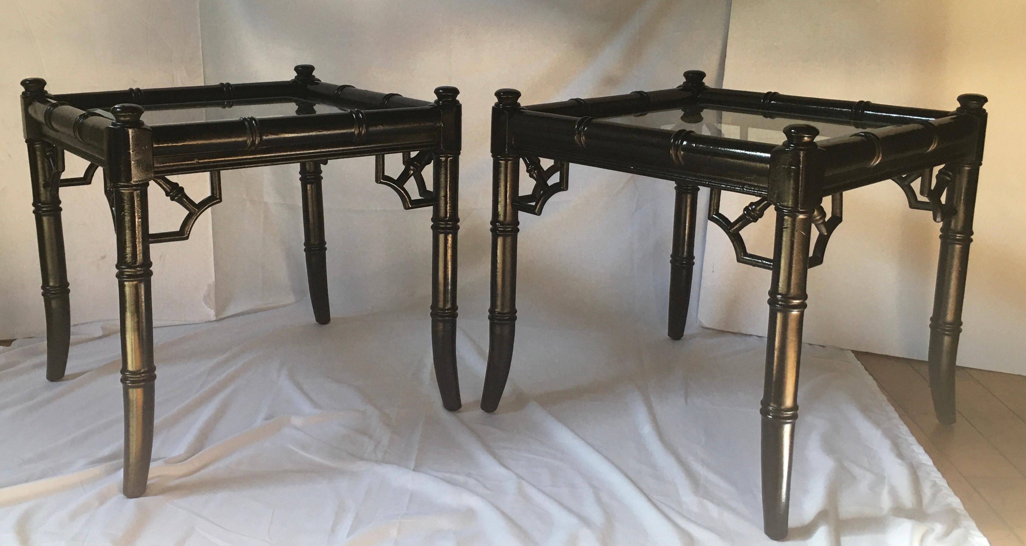 Pair of chinoiserie style faux bamboo reed bunching cocktail tables. These square end or side tables feature gloss black painted wood frames with clear beveled glass inserts and fretwork details. These Hollywood Regency style tables are a nice size