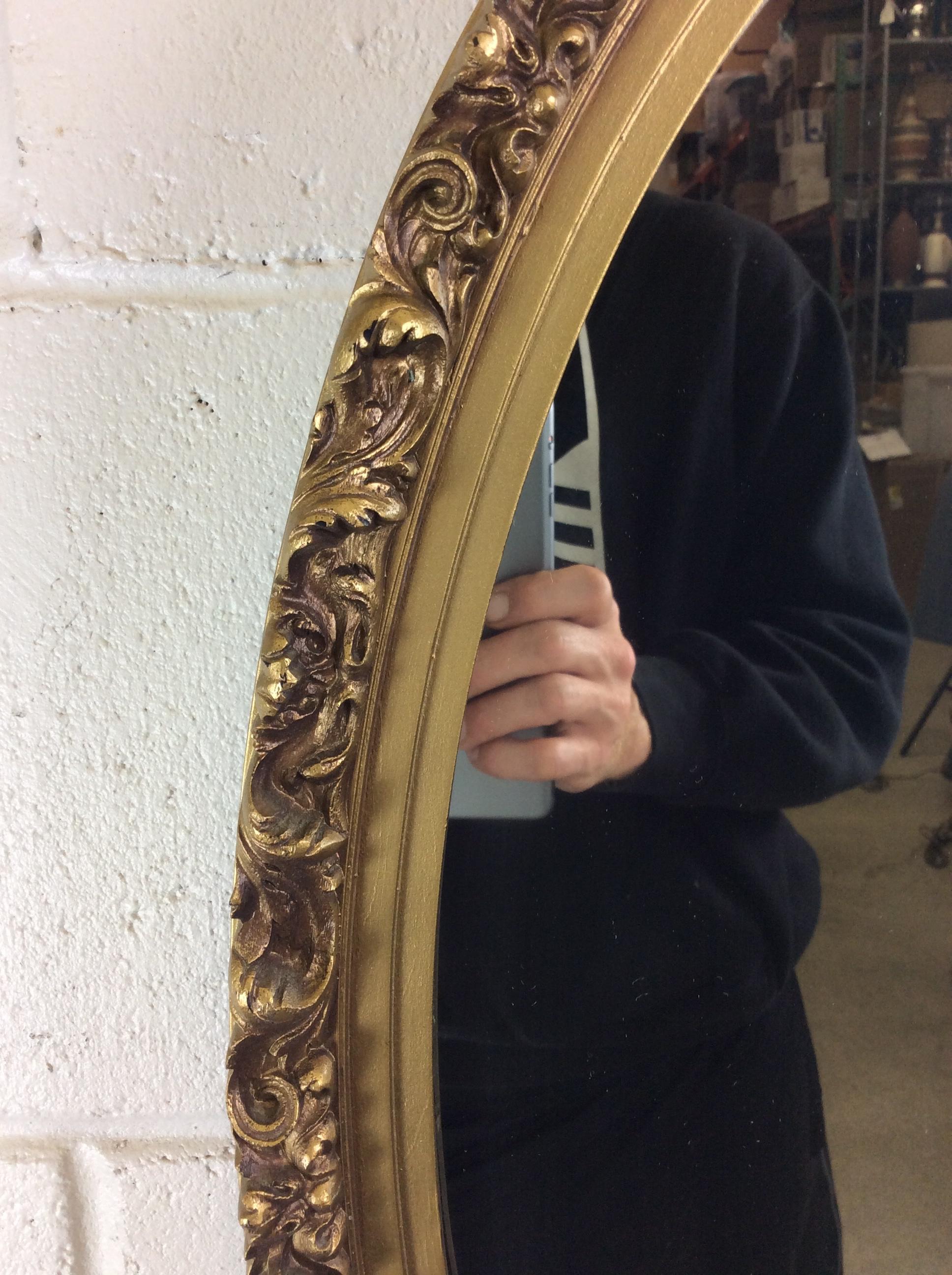 Hollywood Regency style gold floral oval framed wall mirror. The mirror has floral and leaf accents all around the mirror. Hardware is included. No marks.
