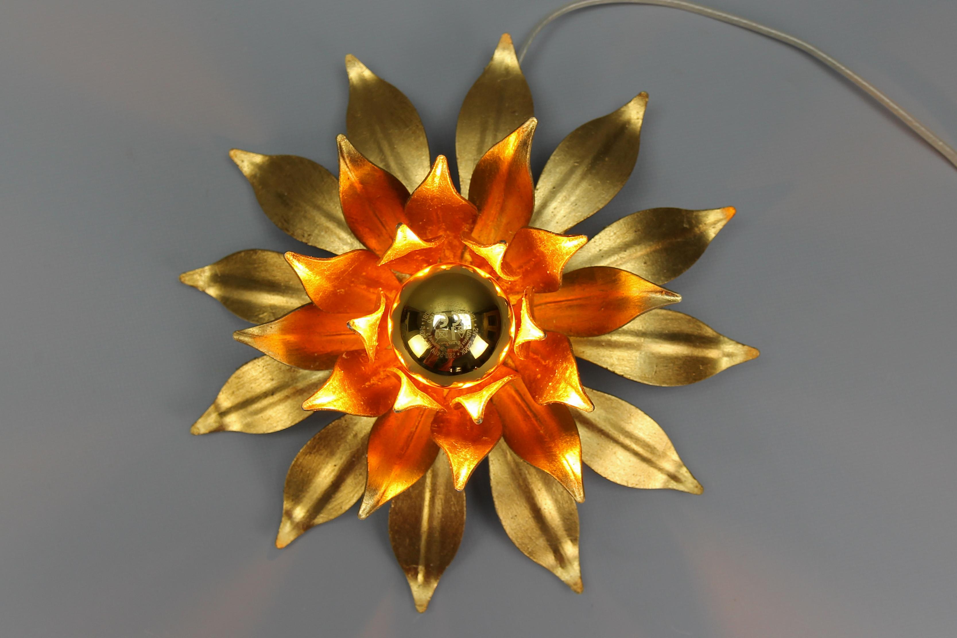 Hollywood Regency style gilt metal flower-shaped flush mount or wall light from the late 1970s, Germany. 
This adorable ceiling lamp features one central light with a socket for an E27 (E26) light bulb. 
The light shining through the stylized