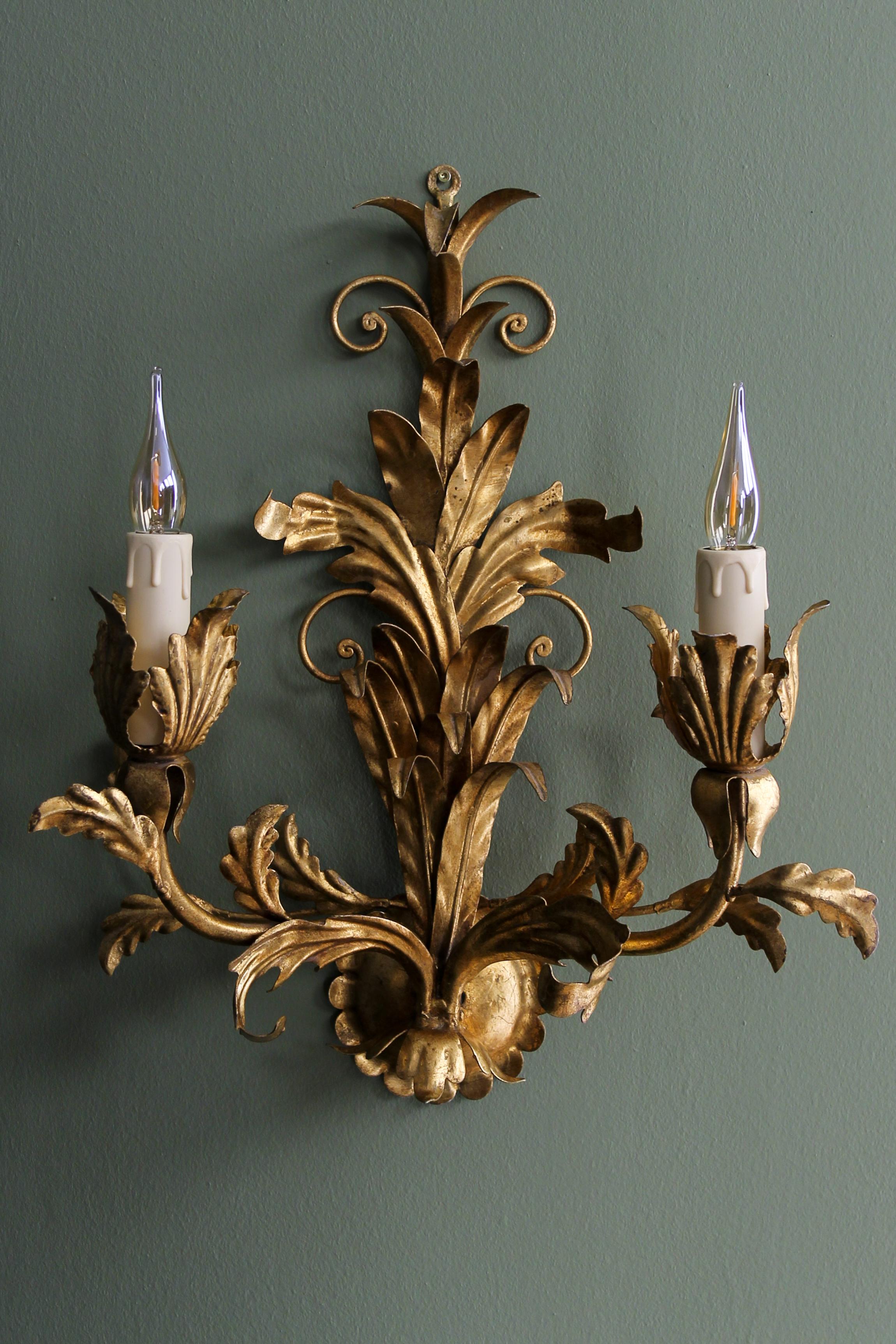 Zweiflammige vergoldete Metallleuchte im Hollywood-Regency-Stil, Hans Kögl zugeschrieben, ca. 1970er Jahre.
Diese schöne Wandlampe aus vergoldetem Metall im Hollywood-Regency-Stil hat Blattmotive und zwei Arme mit Fassungen für