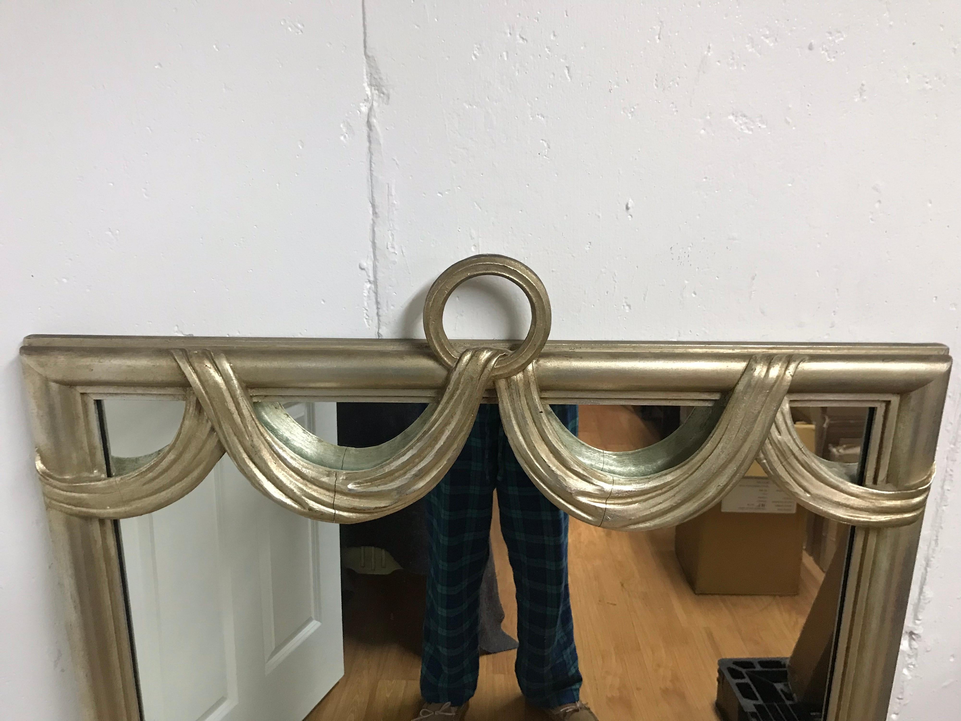This is a wonderful heavy Hollywood Regency style silver/gold giltwood mirror from 1960s 
The swag is a unique design you don’t see very often.