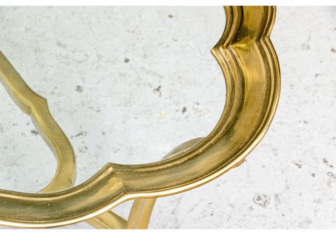 A Hollywood Regency style solid brass cocktail Table with stylish form, scalloped edge, inset glass top and conjoined with a conforming stretcher while resting on well cast feet. The table with good weight, excellent proportions and a light see