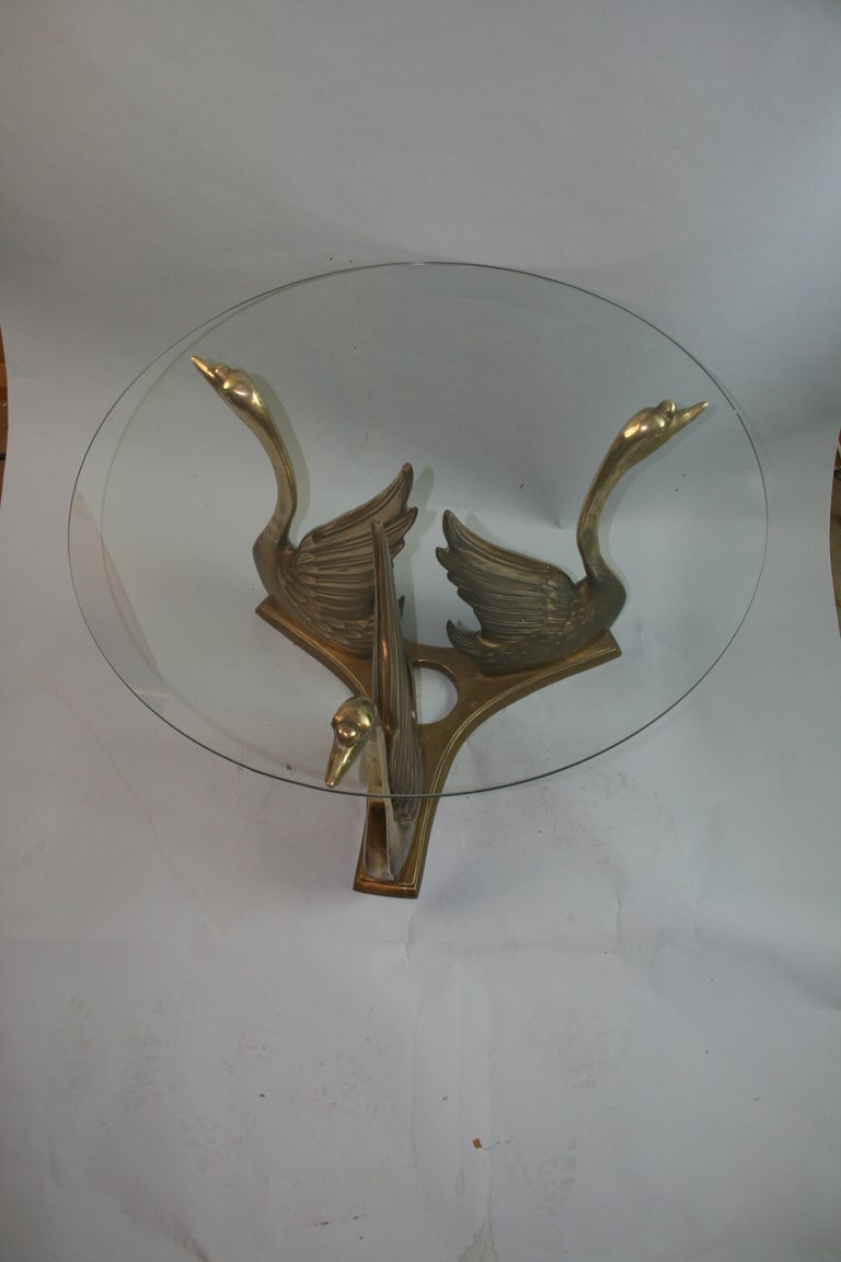 1277 A vintage circa 1970's coffee and coctail table, with round glass top, supported by a trio of swans in brass.
This table beautifully articulates the elegant Hollywood Regency style.
Very good condition with age appropriate patina to the brass.