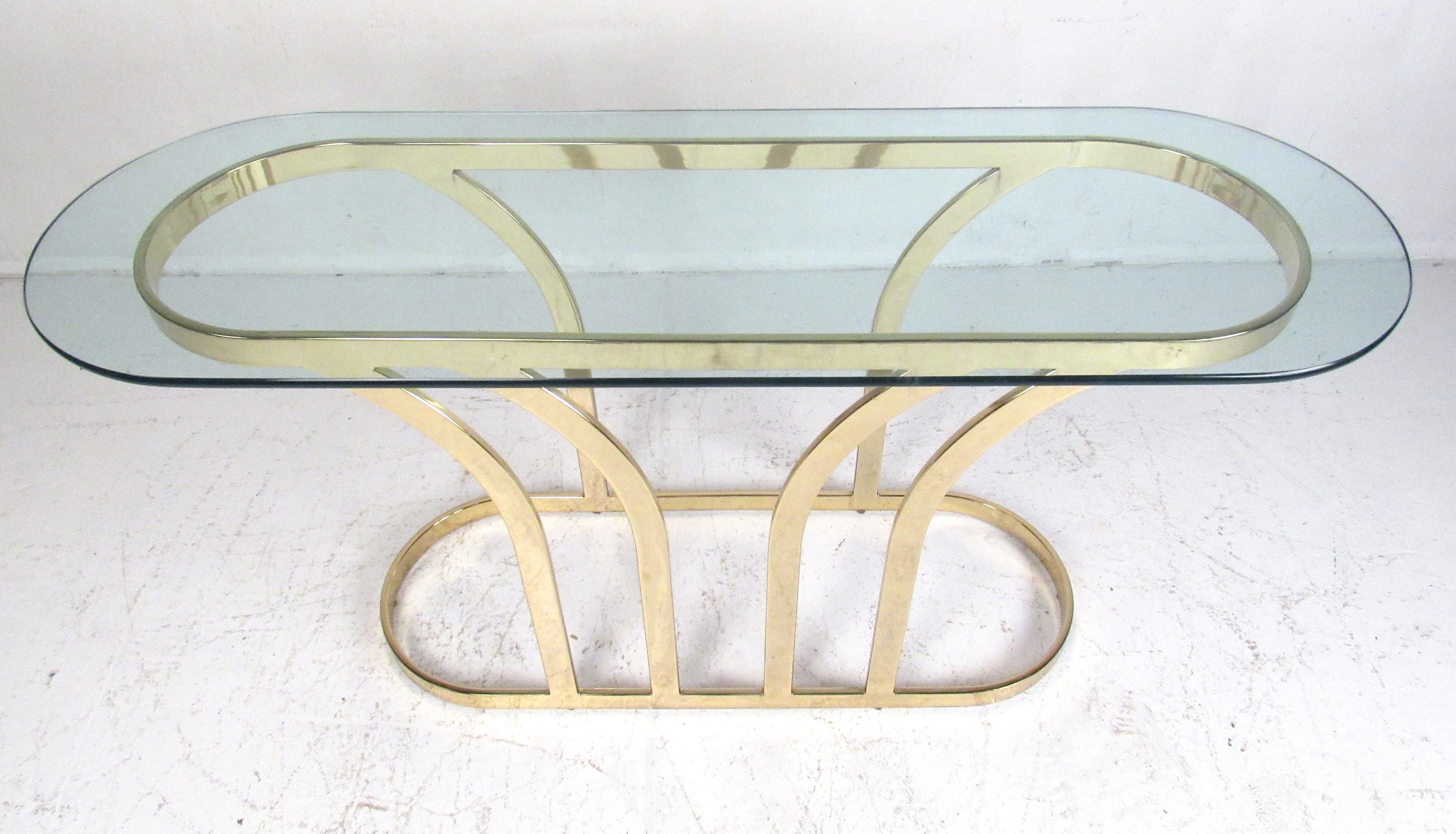 Stylish console table features a racetrack-shaped thick glass top and a brass colored base. Will make a beautiful addition to any Mid-Century Modern or Hollywood Regency setting. Please confirm item location (NY or NJ) with dealer.