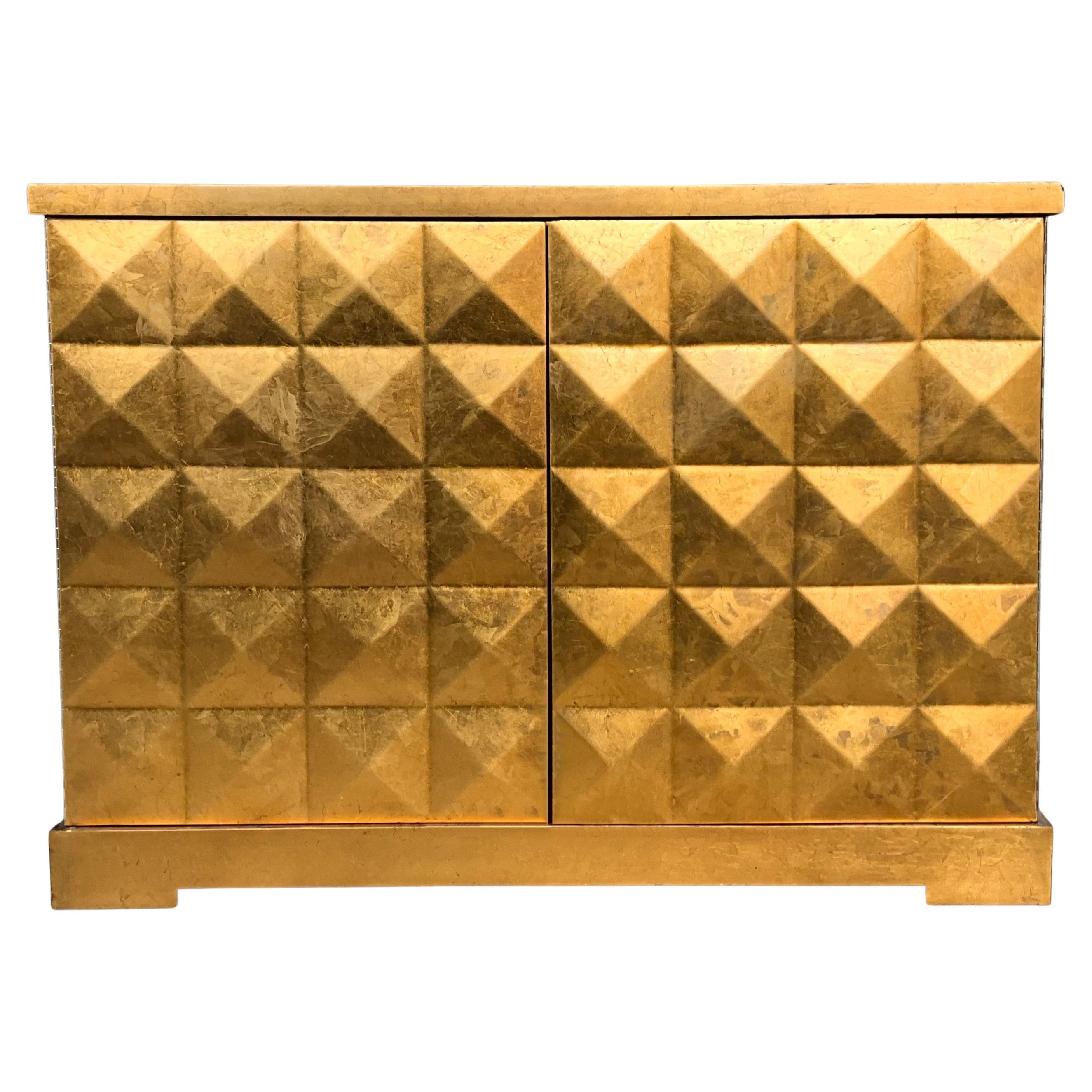 This is a killer piece! It is a Hollywood Regency style gold leaf cabinet designed by Barbara Barry for Baker Furniture. The doors have a raised pyramid design. The interior is a Chinese red with adjustable shelves. It is in very good condition and