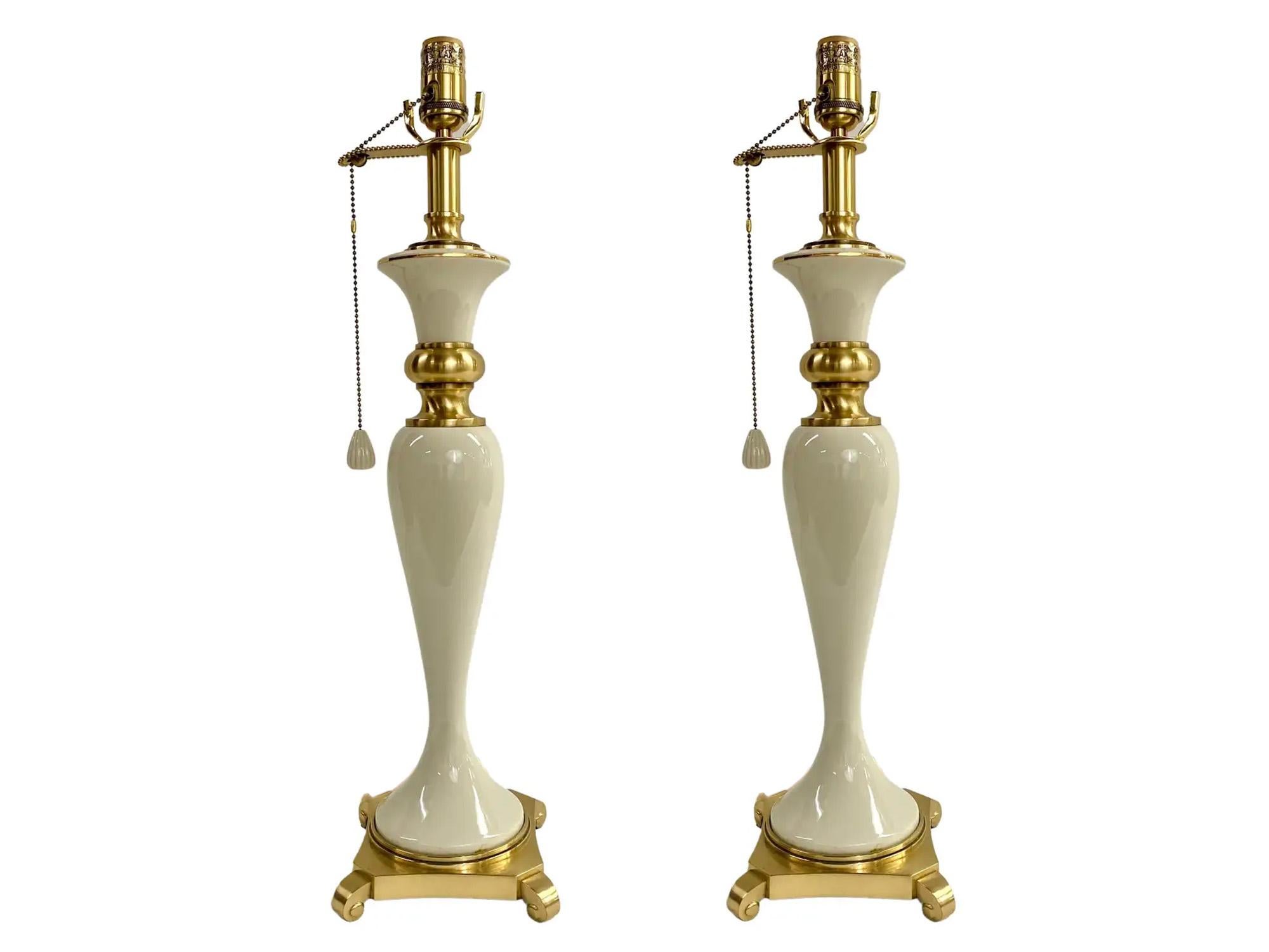 A pair of Hollywood Regency style table lamps by Lenox for Quoizel. The classic style lamps are made of white porcelain and feature beautiful brass trim and base. The lamps are both marked by the base and read