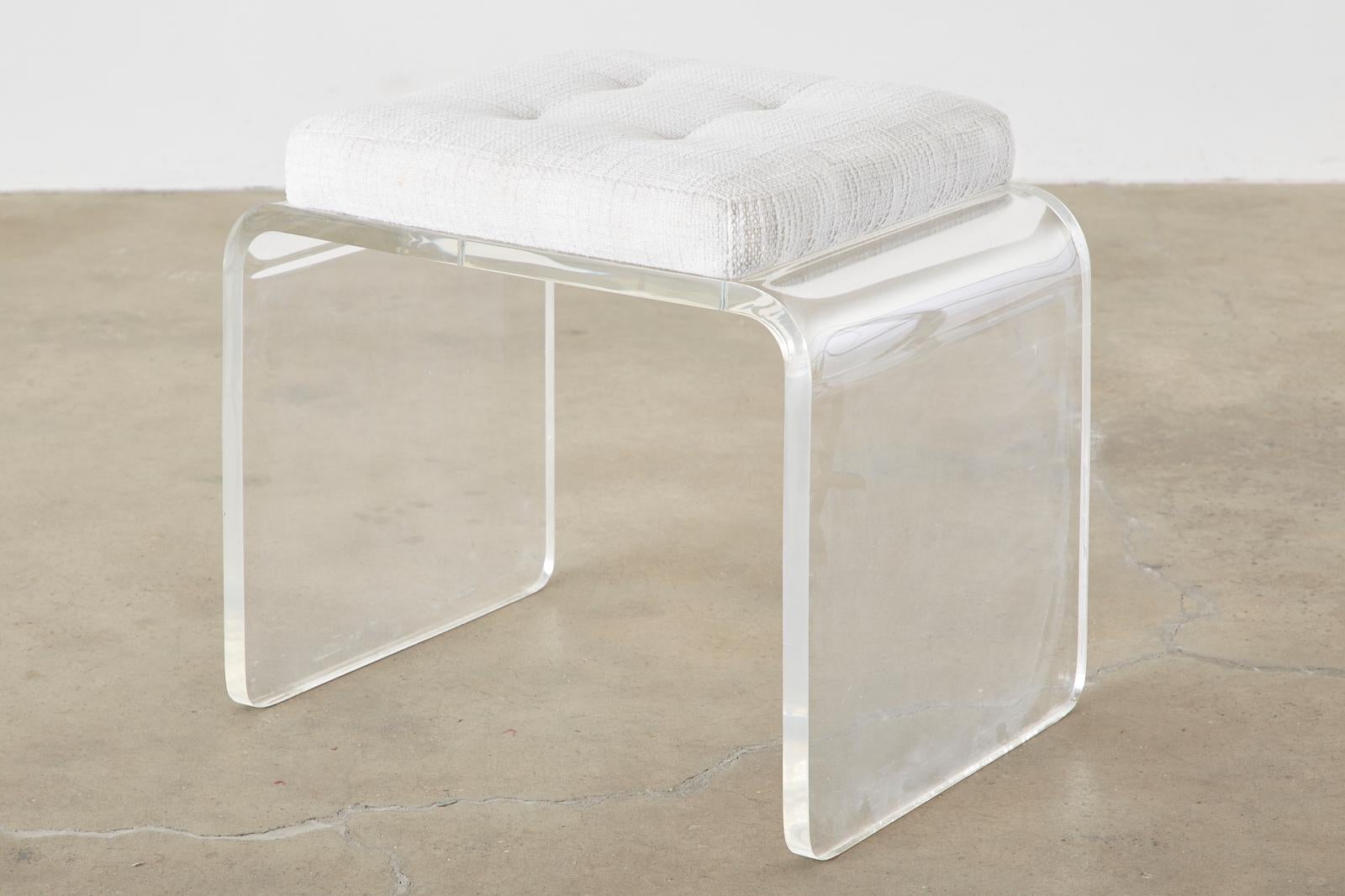 Stylish acrylic Lucite vanity bench or stool having a waterfall form. Features a white Hollywood Regency style upholstered cushion in a white linen material with a subtle tufting. Constructed from Lucite 1 inch thick and bent on the ends to form the