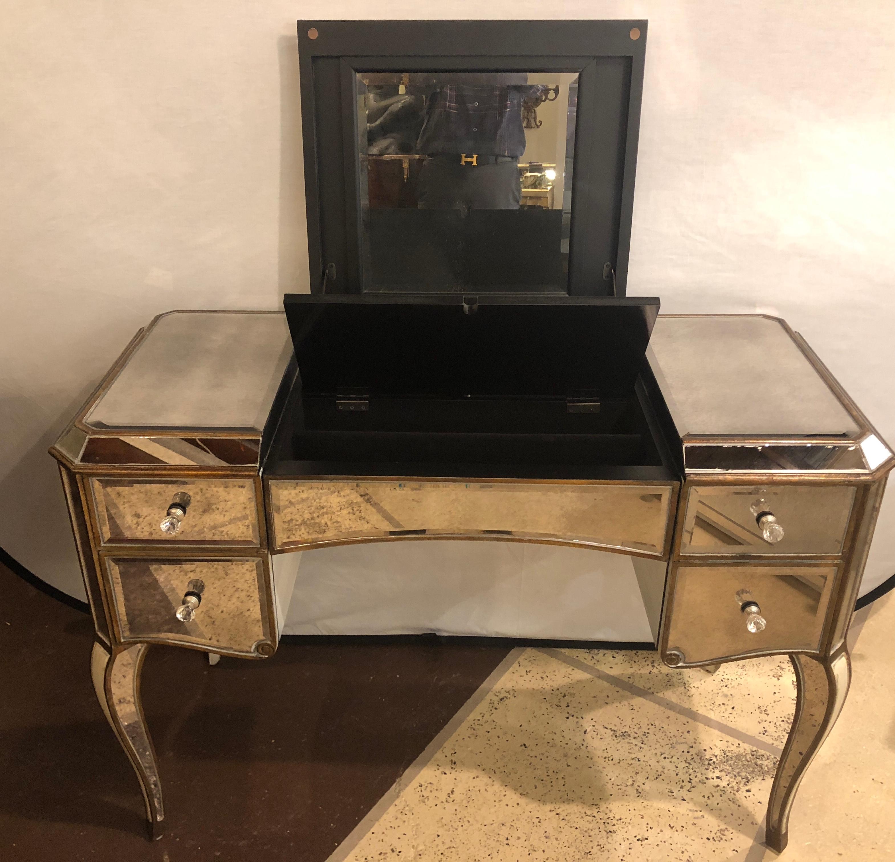 A fine mirrored curved gilt legged five draw vanity accentuated with crystal knobs. The sweeping mirrored legs finely framed in a wooden gilt gold design. The centre flip top drawer having hide away interior compartment, flanked by a group of four