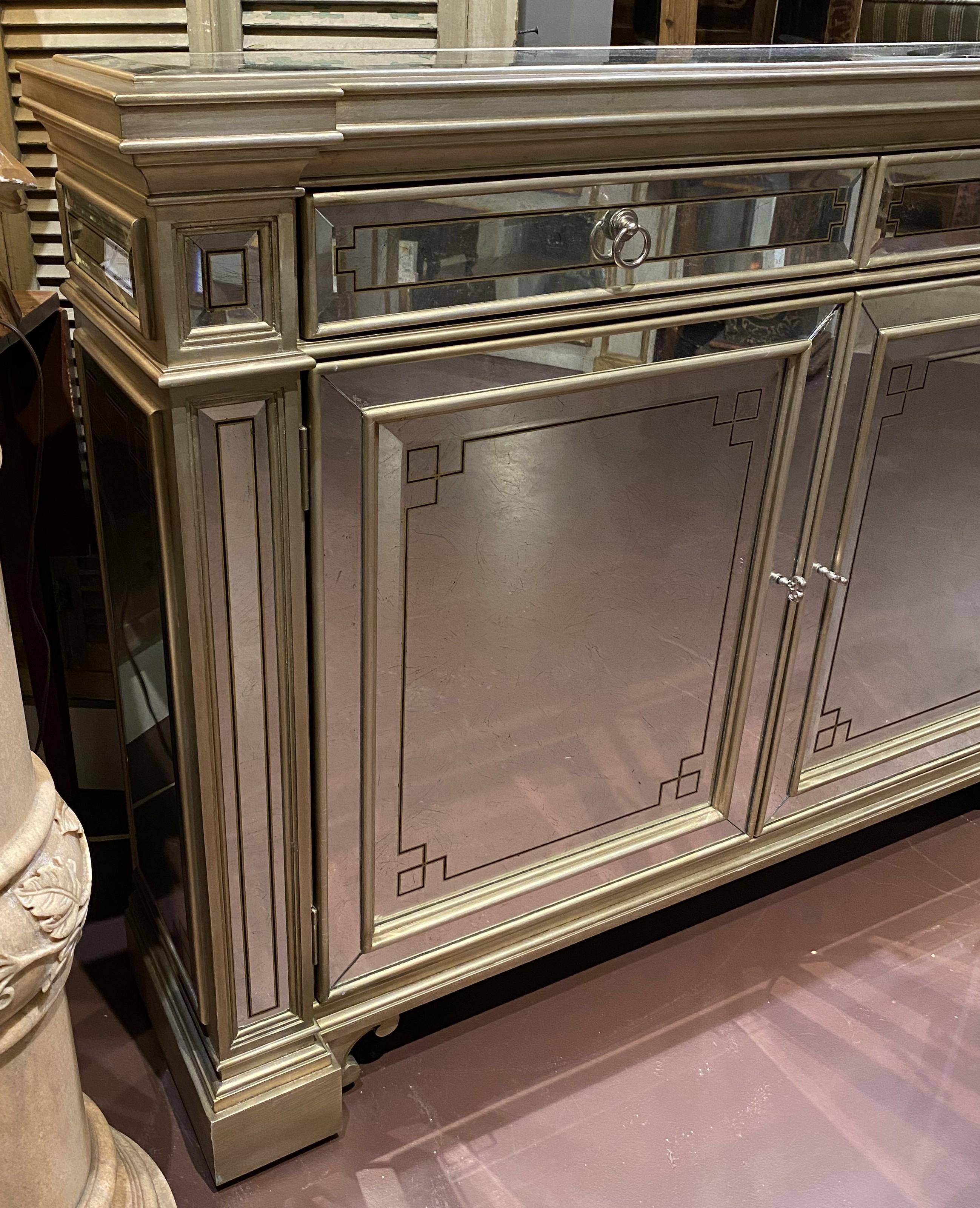 Un raffinato mobile o consolle rettangolare a specchio in stile Hollywood Regency con accenti dorati di Ferguson Copeland Ltd con sede a Morganton, North Carolina, con due cassetti a fregio su due porte a specchio, che si aprono su due ripiani