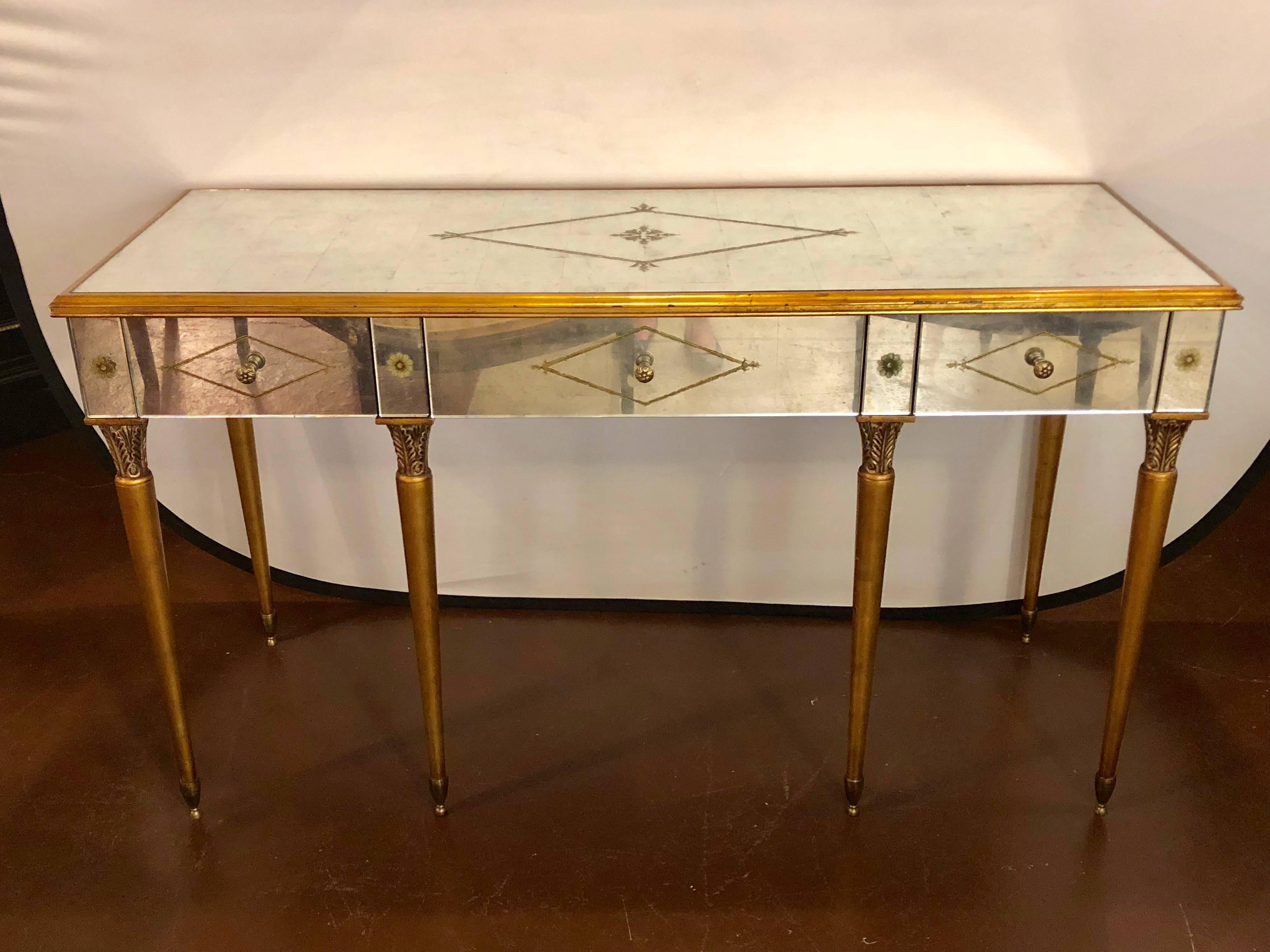 Hollywood Regency style mirrored desk or vanity églomisé decoration by Heritage. Supported by sleek tapering gilt legs having a center diamond designed églomisé silver gilt drawer flanked by matching side drawers. The mirrored top with gilt diamond