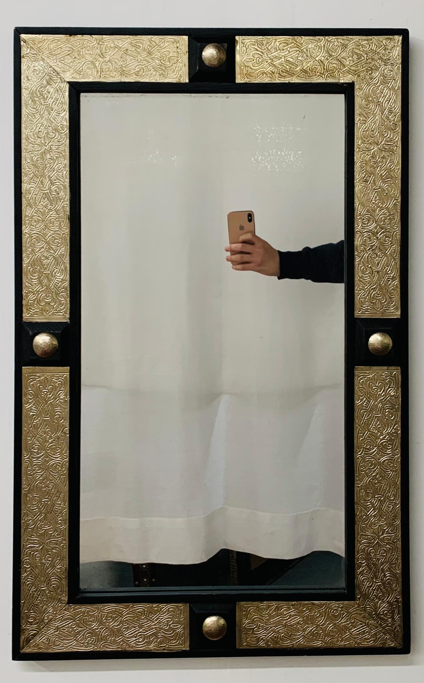 Miroir marocain de style Hollywood Regency ébonisé sur laiton, 
Le miroir présente un cadre rectangulaire en bois ébénisé flanqué d'un insert en laiton conçu à la main dans un style filigrane avec des décorations de boutons en laiton sur fond