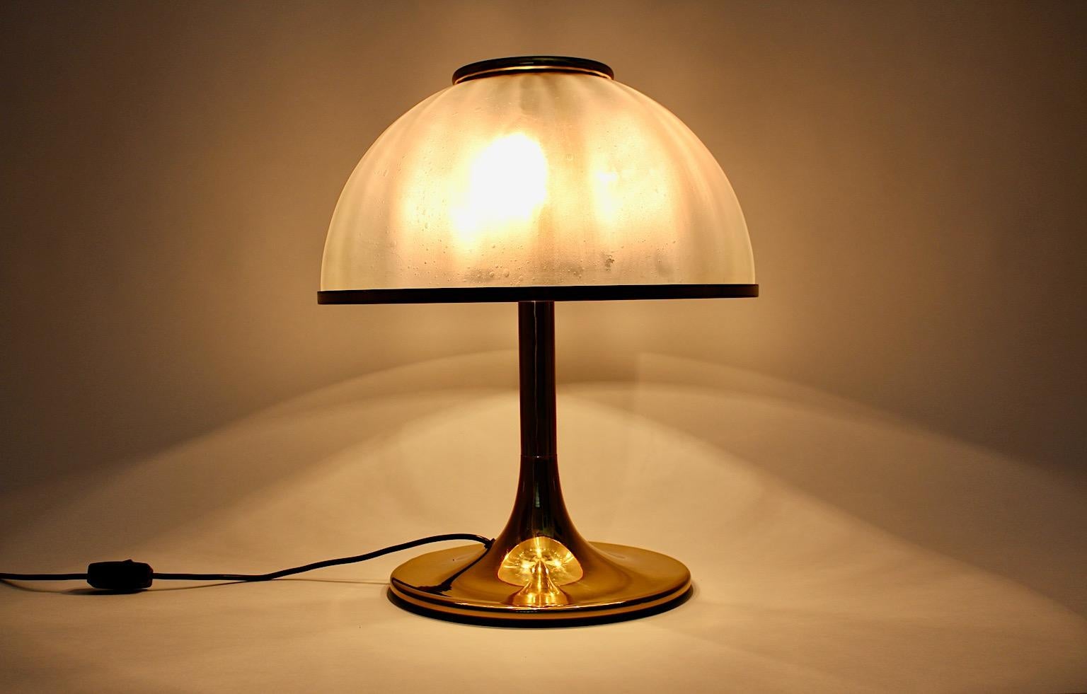 Hollywood Regency Style vintage mushroom like table lamp from brass and glass, Italy 1970s.
While the glass dome from iridescent glass shows nice glass bubbles and a brass trim, the brass base features a circular base trumpet like.
Throughout its