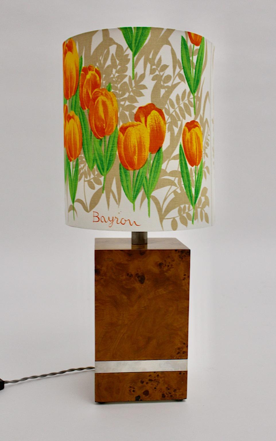 Lampe de table vintage de style Hollywood Regency en placage de bois de peuplier et détails chromés à la base rectangulaire.
L'abat-jour récemment réalisé à la main à partir d'un délicat tissu batiste présente des fleurs dans des couleurs vives