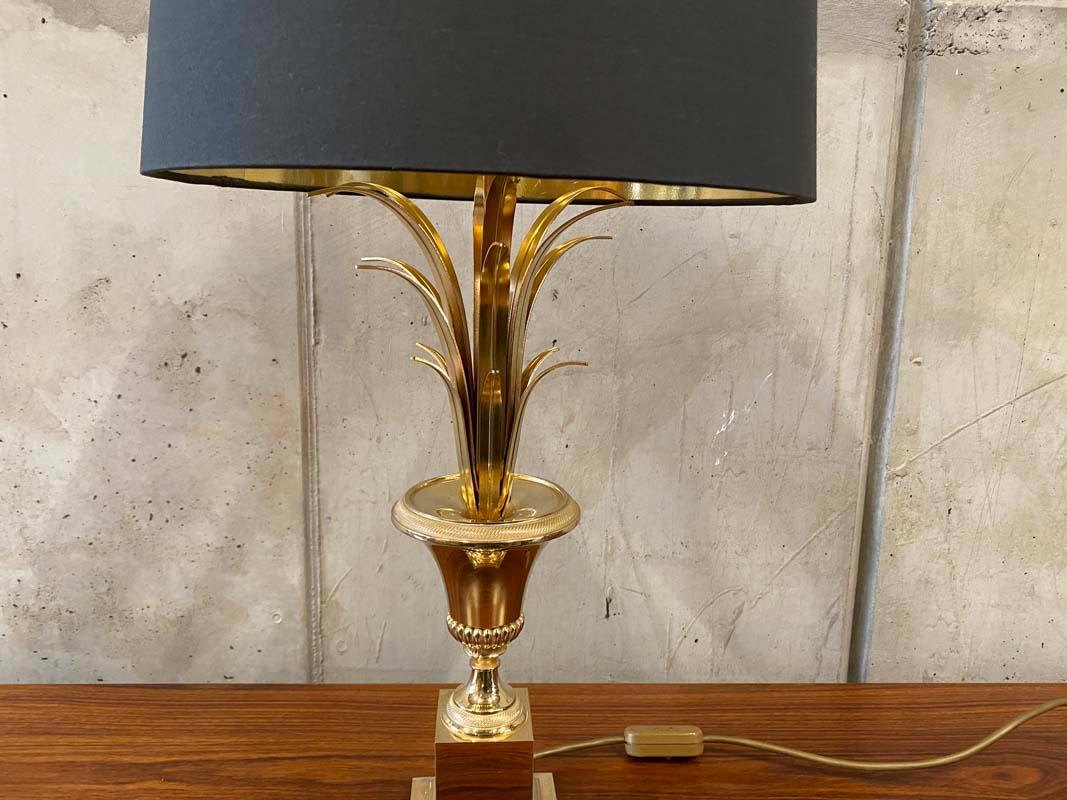 I would attribute this particular Hollywood Regency style table lamp to Maison Jansen. It stands on a gilded base in the shape of a palm tree and must be from the 1970s. The new lampshade is made of linen in anthracite and shiny gold from the inside
