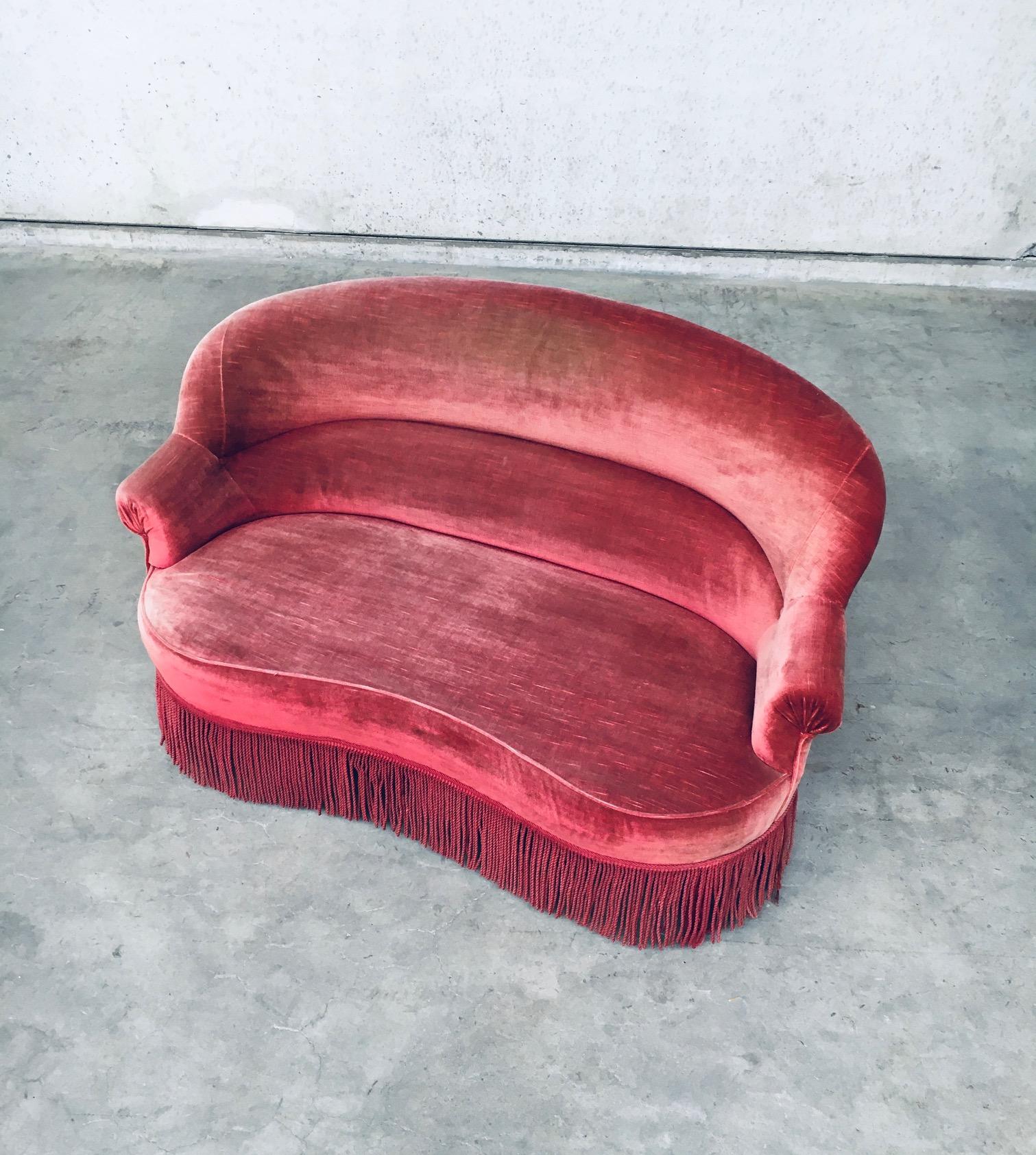Vintage mid-century Design Hollywood Regency style velvet 2 seat loveseat sofa with fringe in red / pink, made in Belgium 1950's. In the style of the 1920's / 30's boudoir sofa seats. Curved back and seat. Feet are also covered in velvet fabric. In