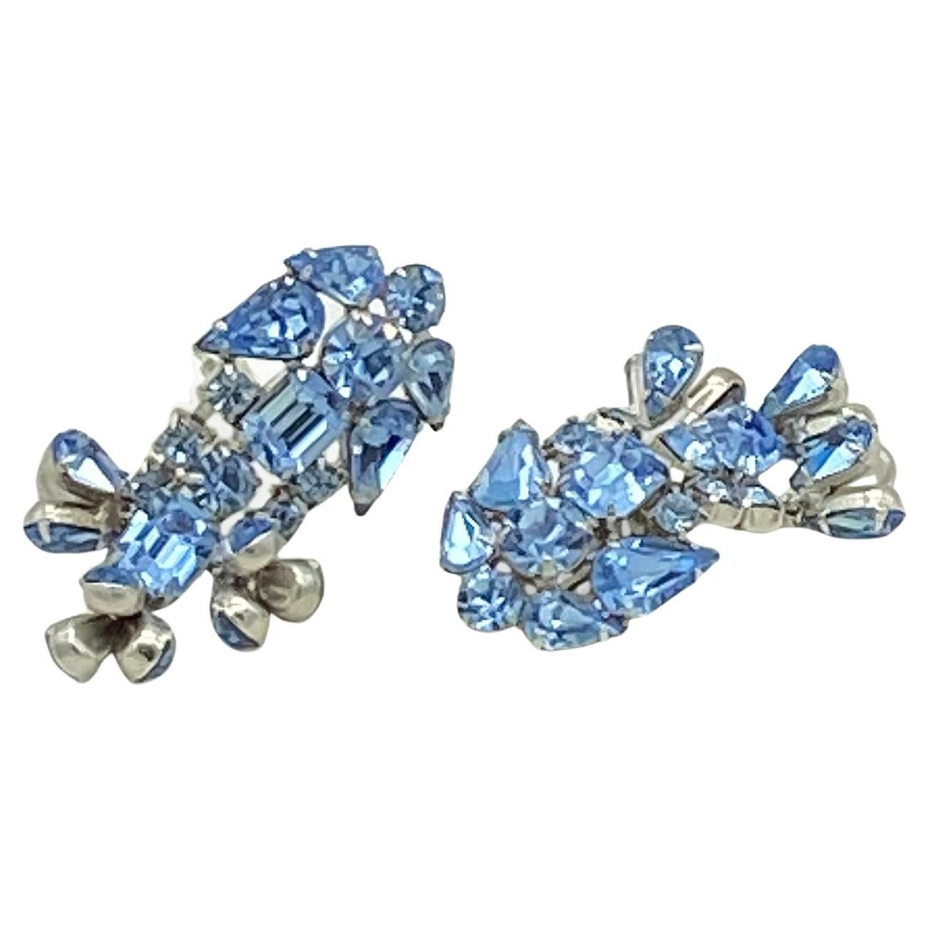 This is a pair of  Hollywood Regency Style rhinestone dangle earrings  prong set with multiple different shaped French blue rhinestones on rhodium plated metal. These clip back earrings have an unusual triple 3 teardrop cluster dangling design.