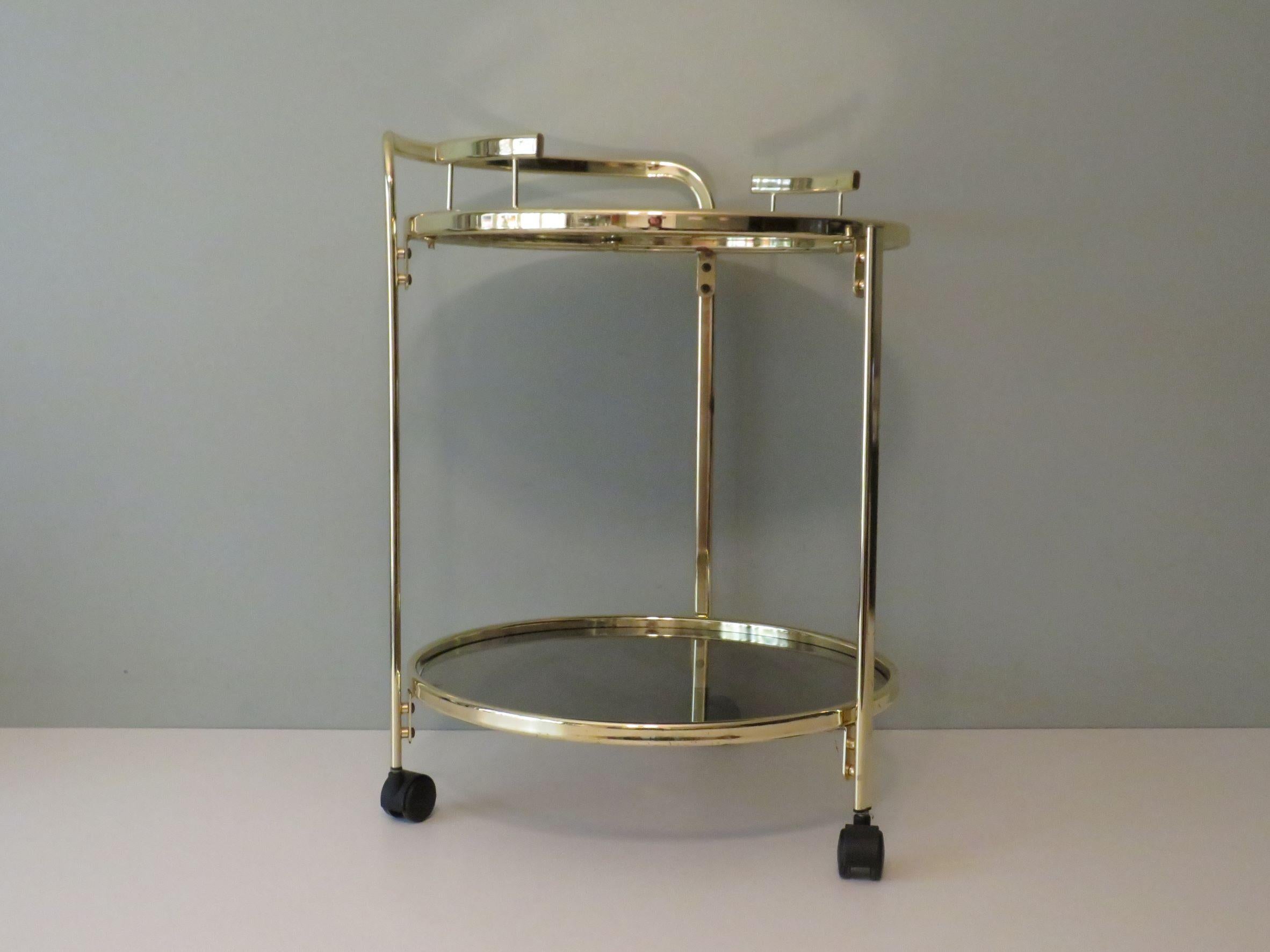 Round gold-plated metal serving trolley with wheels and removable tray.
The smoked glass top at the bottom is at a height of 14 cm and
the removable tray with mirror glass is located at 56 high and has 2 handles.
The height of the serving trolley