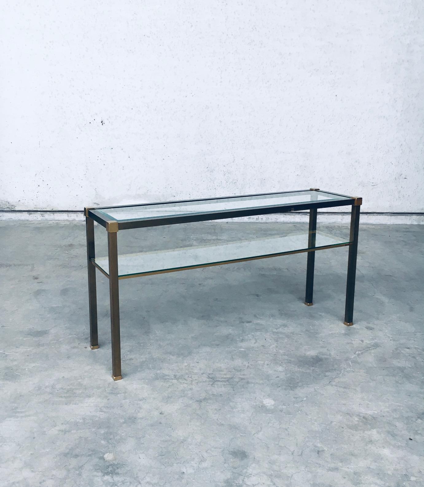 Vintage Design Hollywood Regency Style Slender Two Tier Console. Made in the Netherlands, 1970's period. 2 tone brass construction with glass inlay. The top glass has beveled edges. Sleek and minimalist in design. This comes in very good condition,