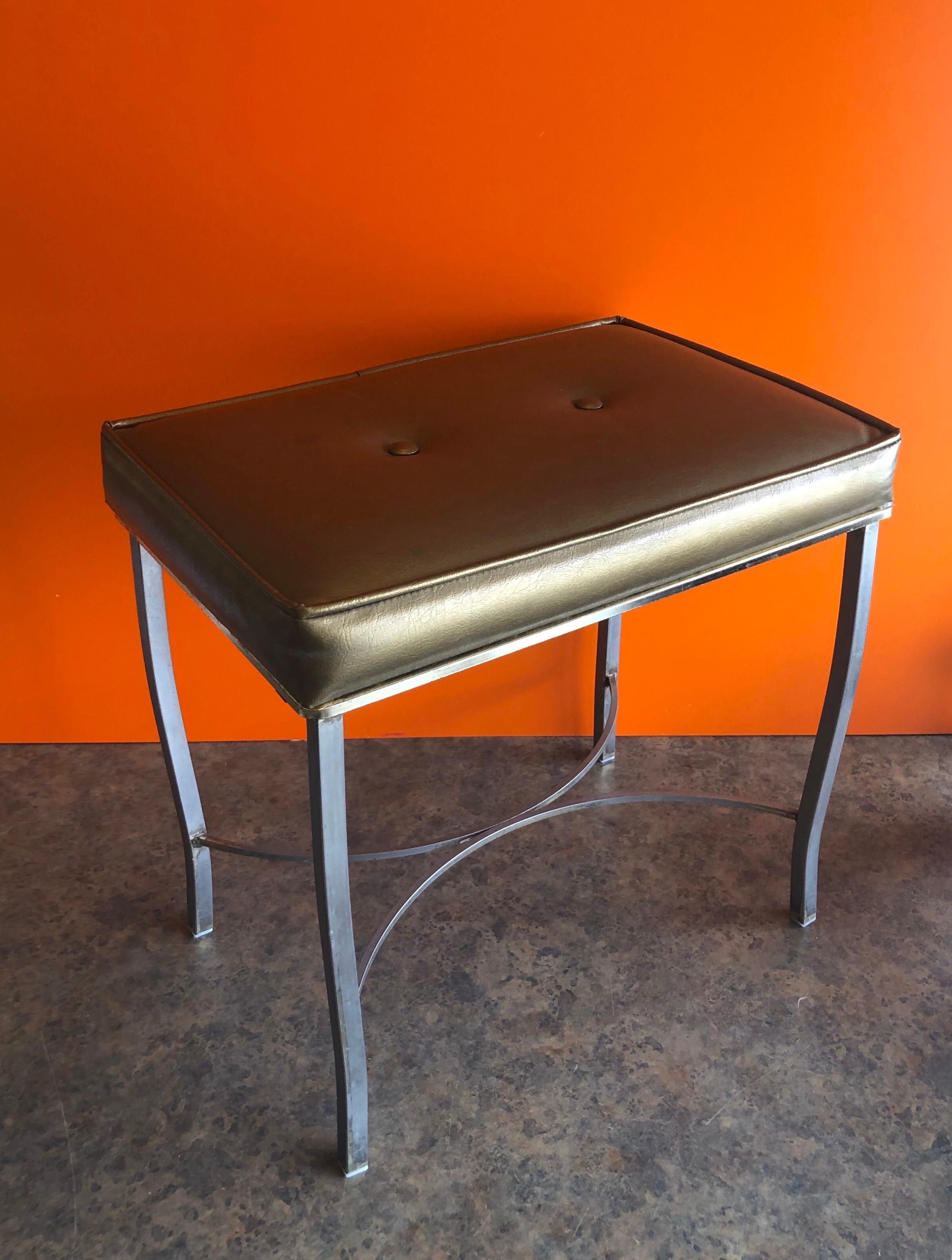 Hollywood Regency style metal and gold naugahyde vanity stool / ottoman by George Koch & Sons, circa 1960s. The piece is in good vintage condition; solid and stable with curved legs and a stretcher accent. There some scratches, wear and patina to