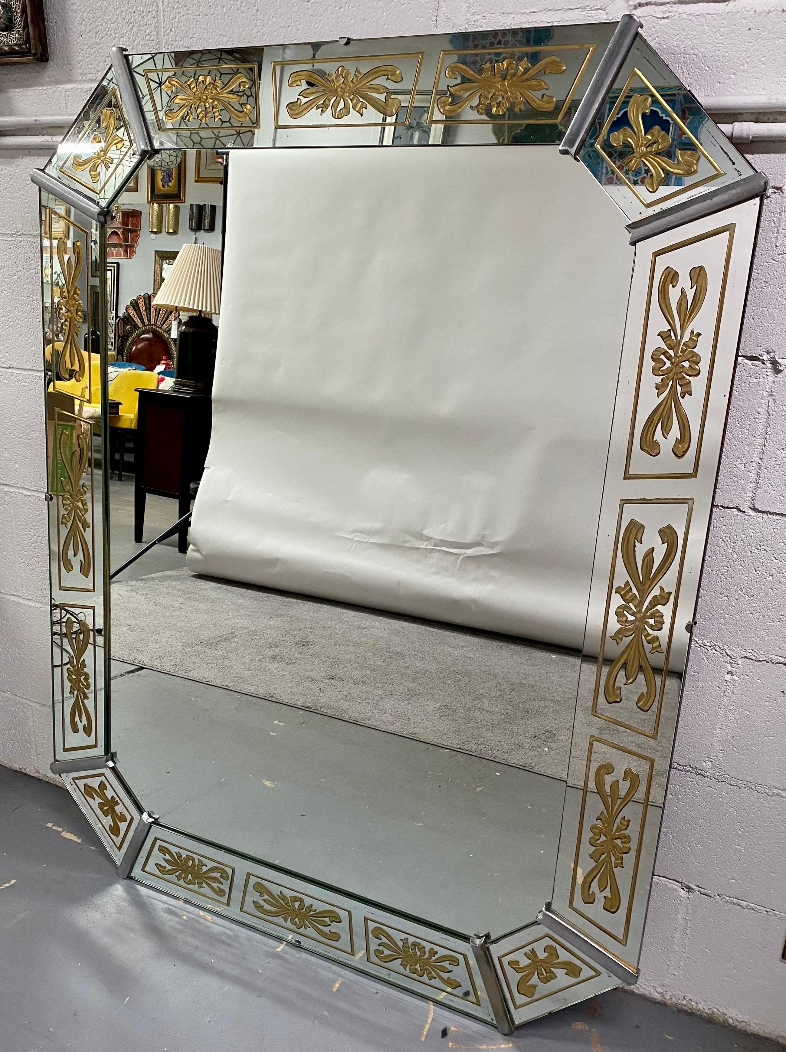 An elegant Hollywood Regency style Venetian large mirror. The mirror features an octagon shape and is quite sturdy and heavy. The frame is made of 8 individual mirrored panels each is finely and artistically etched in gold to reveal a beautiful bows