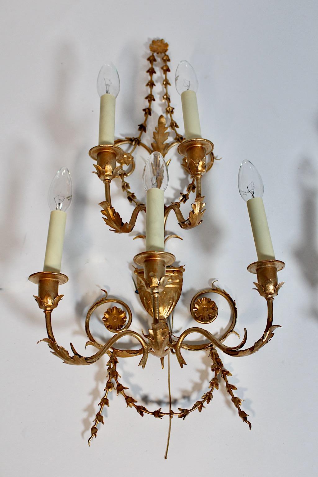 Hollywood Regency Style vintage pair duo sconces or wall lights from gilt metal 1970s Italy.
A richly decorated pair of sconces showing blossom garlands, leaves and vessel with 5 arms and 5 E 14 sockets. Easy to hang up on the upper end of the
