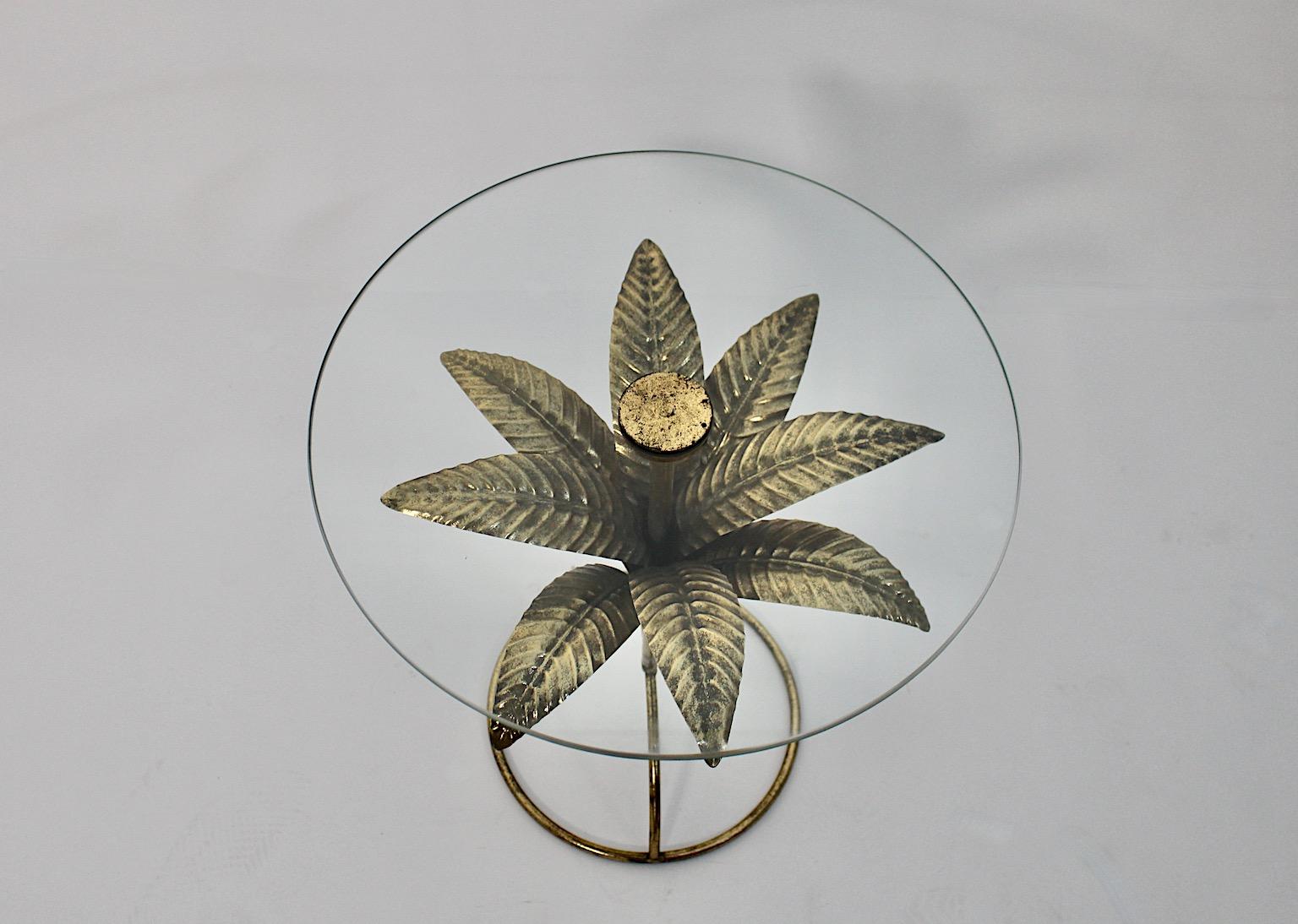 Hollywood Regency Style vintage circular like coffee table or side table from clear glass and golden metal base with golden leaves.
A stunning side table or coffee table with a circular like base featuring golden leaves or palm tree with a clear