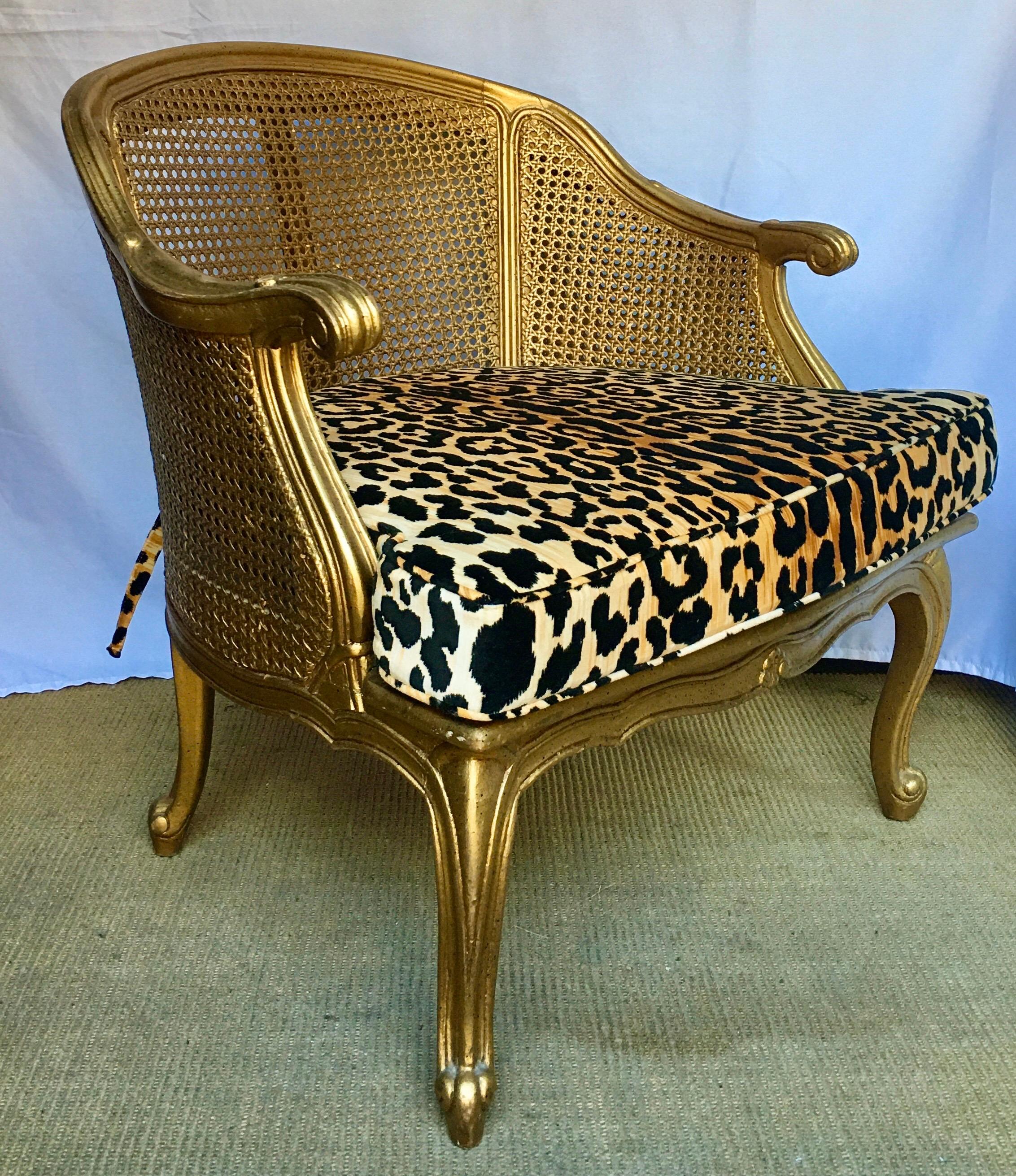 Hollywood Regency style arm accent chair with gilt painted frame, curved cabriolet legs, and cane back/sides. Back and sides of chair are double caned. New custom seat cushion upholstered in a leopard animal print velvet. Chair labeled 