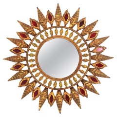 Espejo Hollywood Regency Sunburst en metal dorado y detalle de cristal rojo, años 50