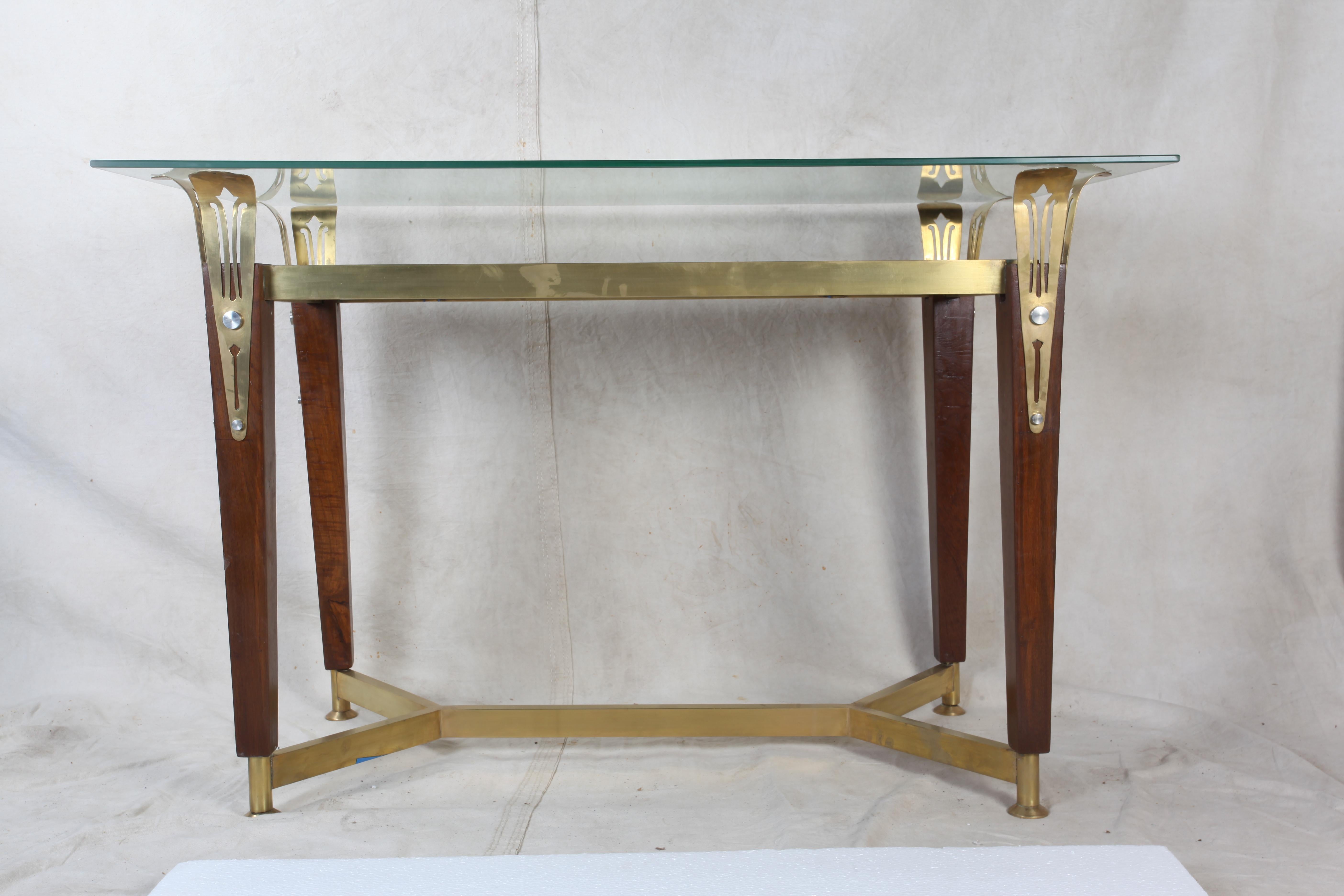 In that Classic, glamorous era of the early-mid 1900s, a lovely console table or desk with teak, brass and glass details. The legs are a tapered teak wood with brass feet and cross bars and cut brass tabletop supports. There is a mirror recessed in